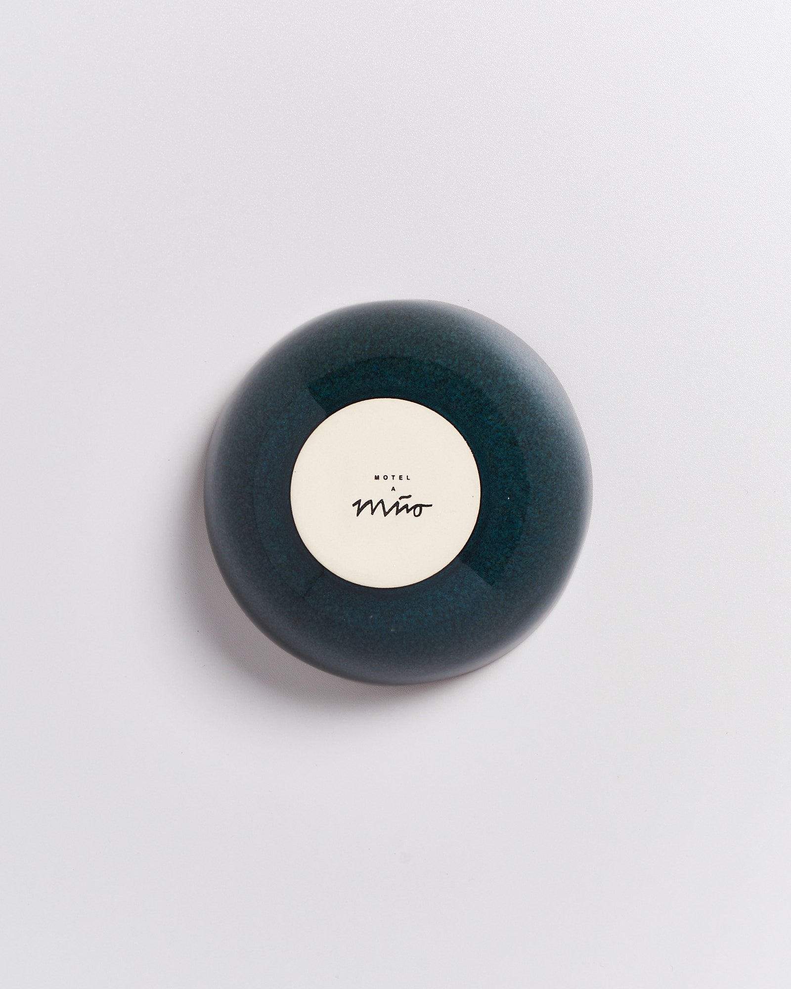 Dunkelblauer runder Seifenspender mit einem weißen Etikett, auf dem in schwarz "HOTEL MIRÓ" steht.