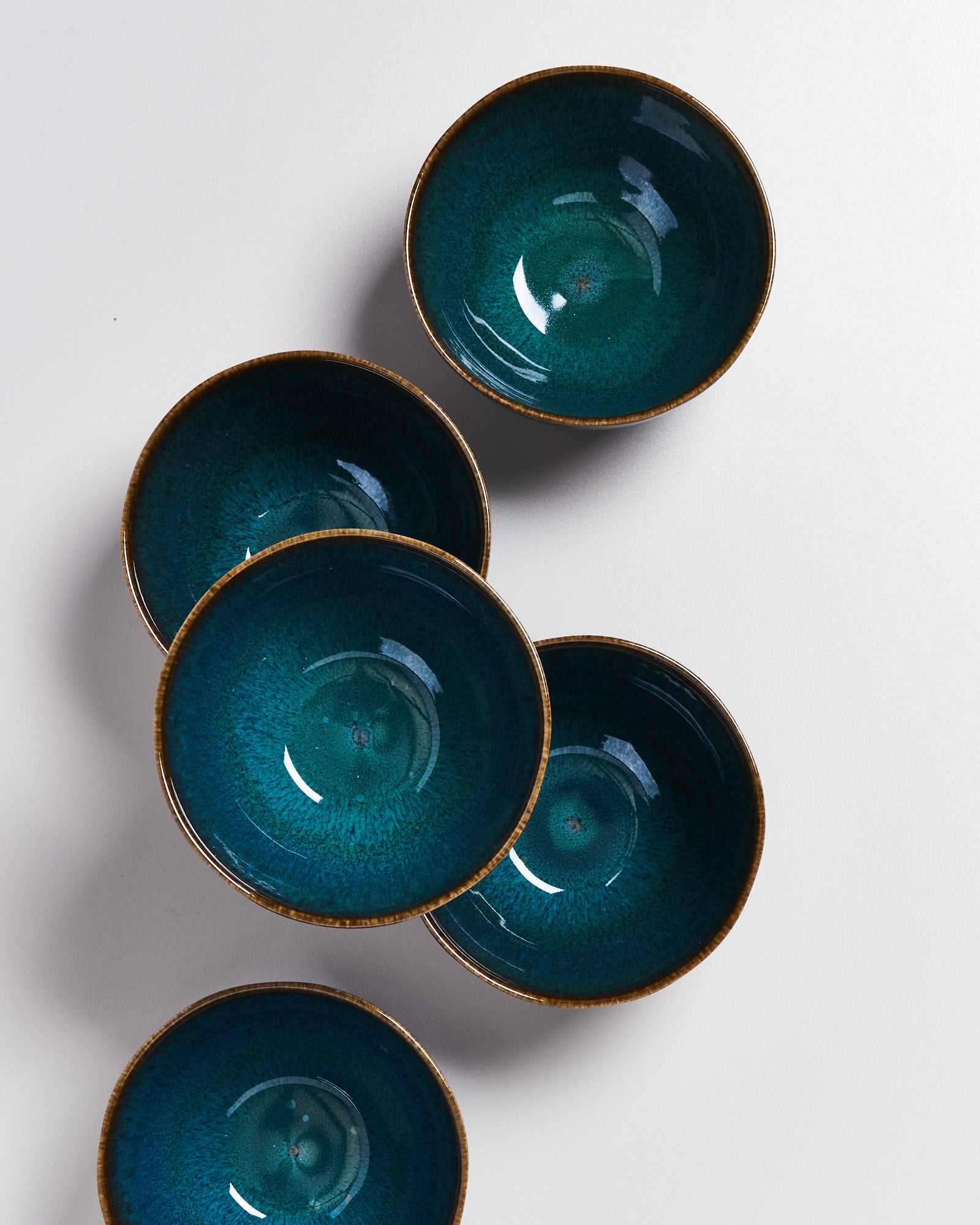 Fünf türkisfarbene, runde Schalen mit braunem Rand auf weißem Untergrund angeordnet.