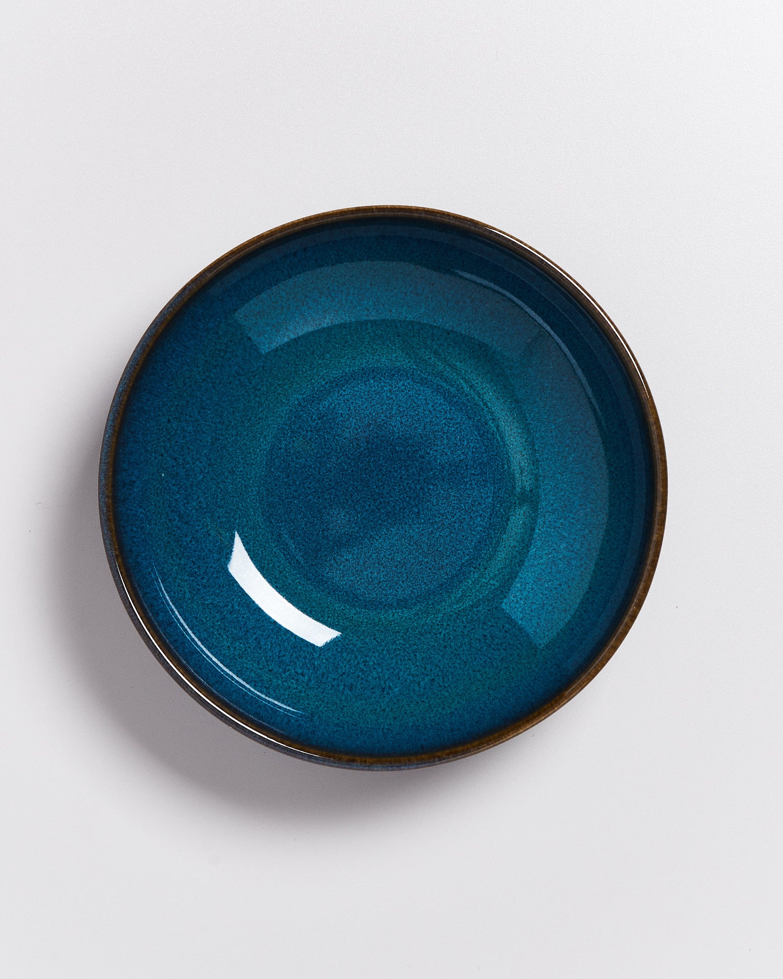 Runder, blauer Keramikteller mit leichtem Glanz auf einer weißen Oberfläche.