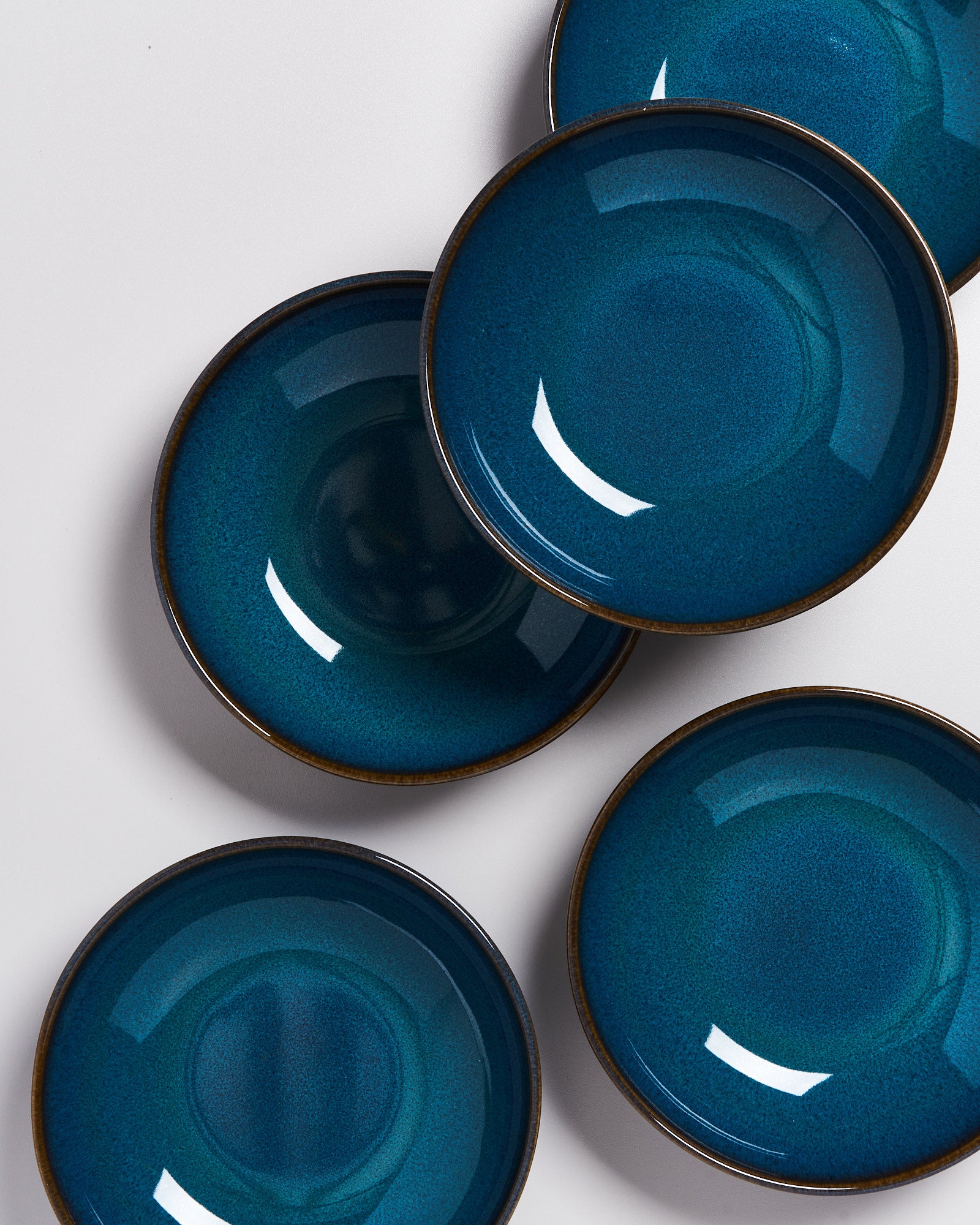 Fünf blaue Teller mit dunklem Rand liegen auf einem weißen Untergrund.