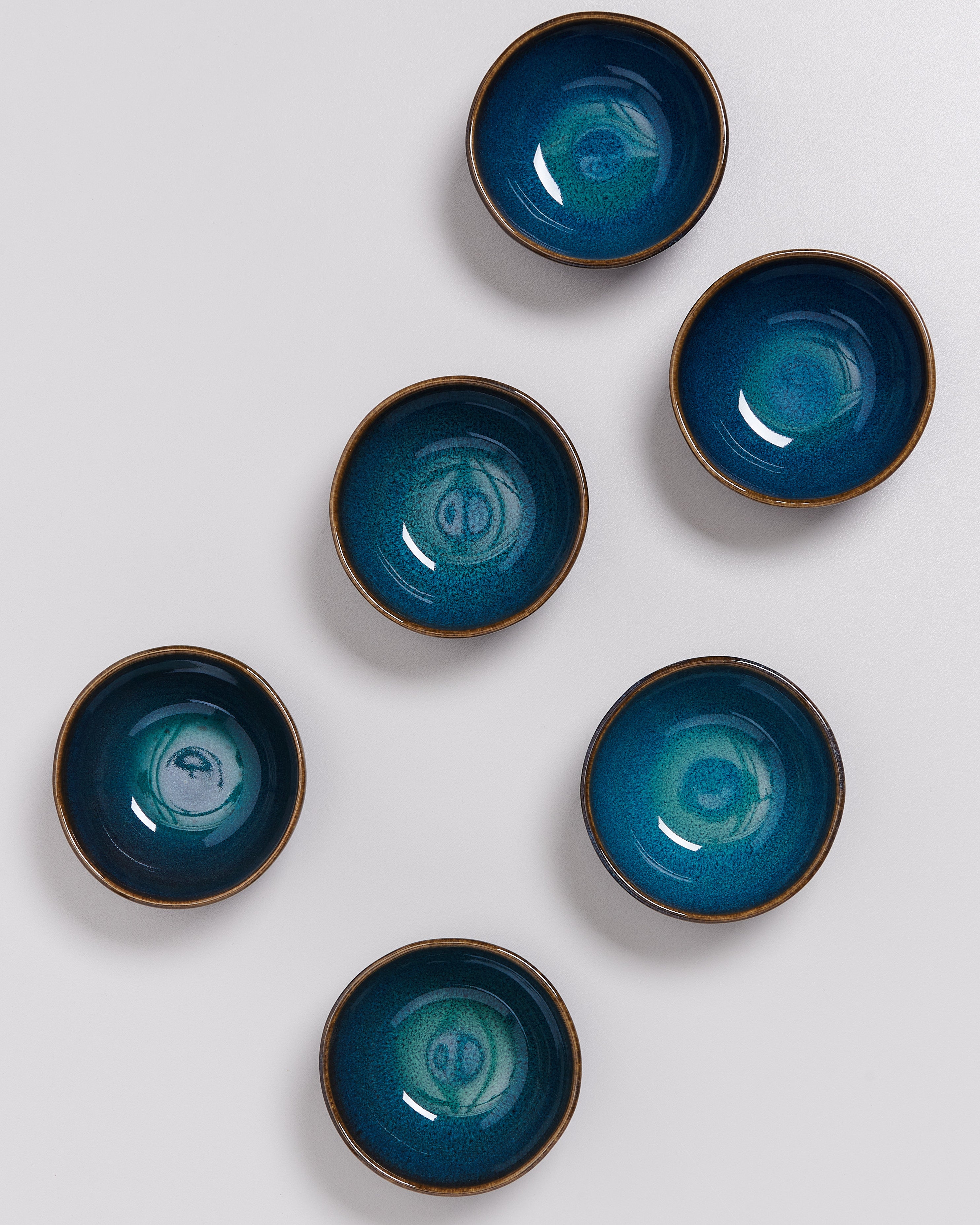 Sechs blaue runde Schalen mit grünem Farbverlauf liegen auf weißem Hintergrund in unregelmäßiger Anordnung.