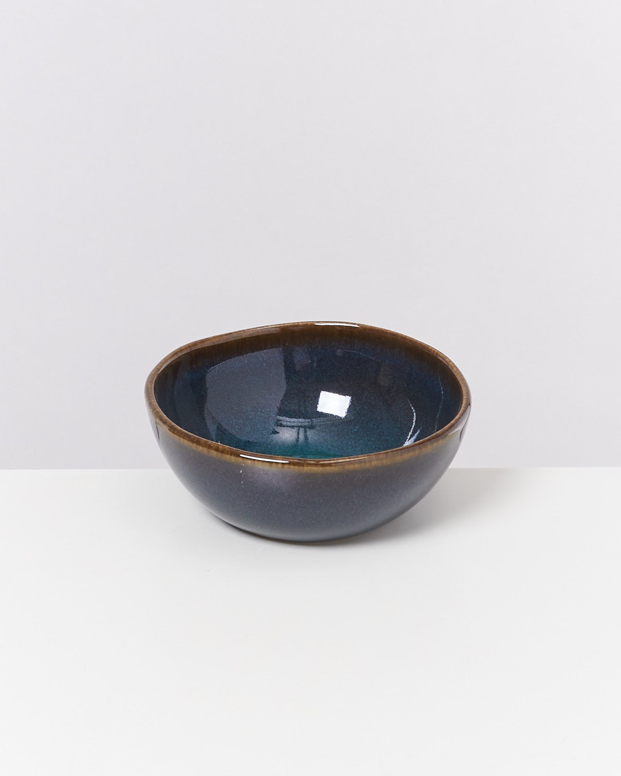 Blaue Keramikschüssel mit braunem Rand auf einem weißen Hintergrund.