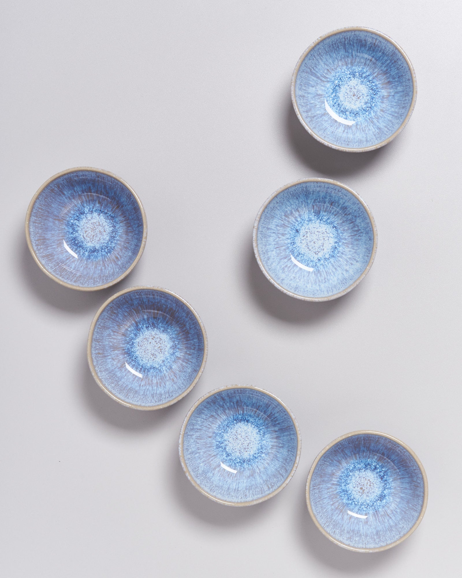 Sechs blaue Keramikschalen mit radialem Muster sind auf einem grauen Hintergrund angeordnet.