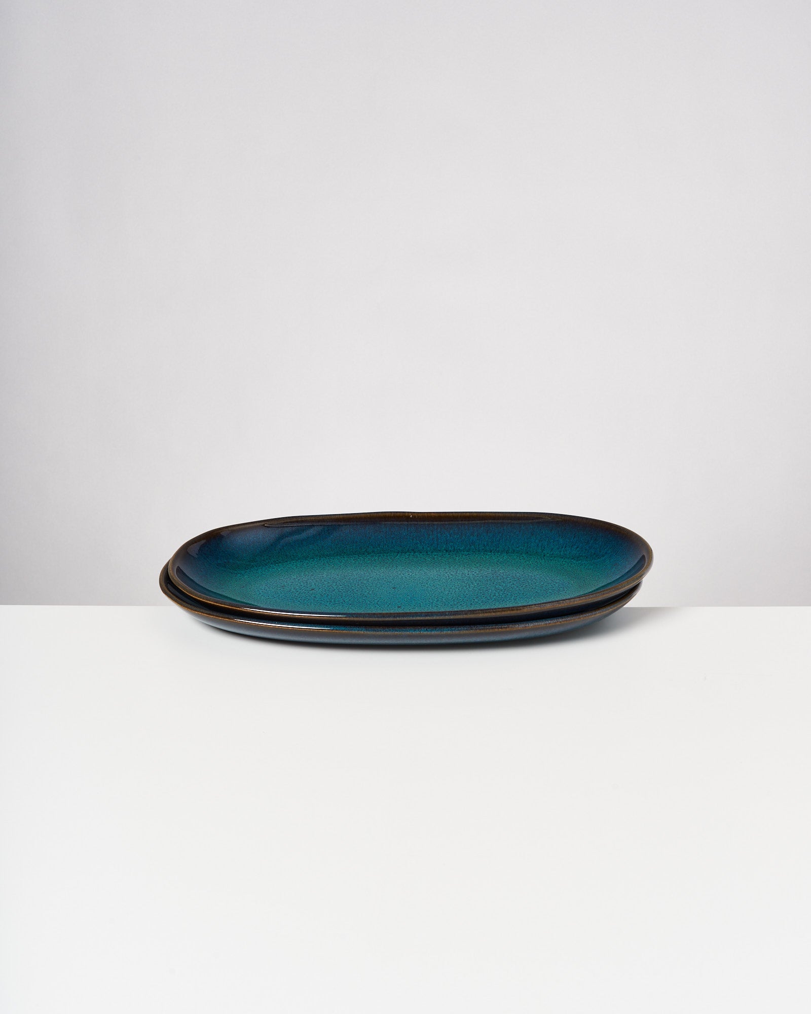 Zwei ovale, blaugrüne Teller auf einem weißen Tisch vor einem grauen Hintergrund.
