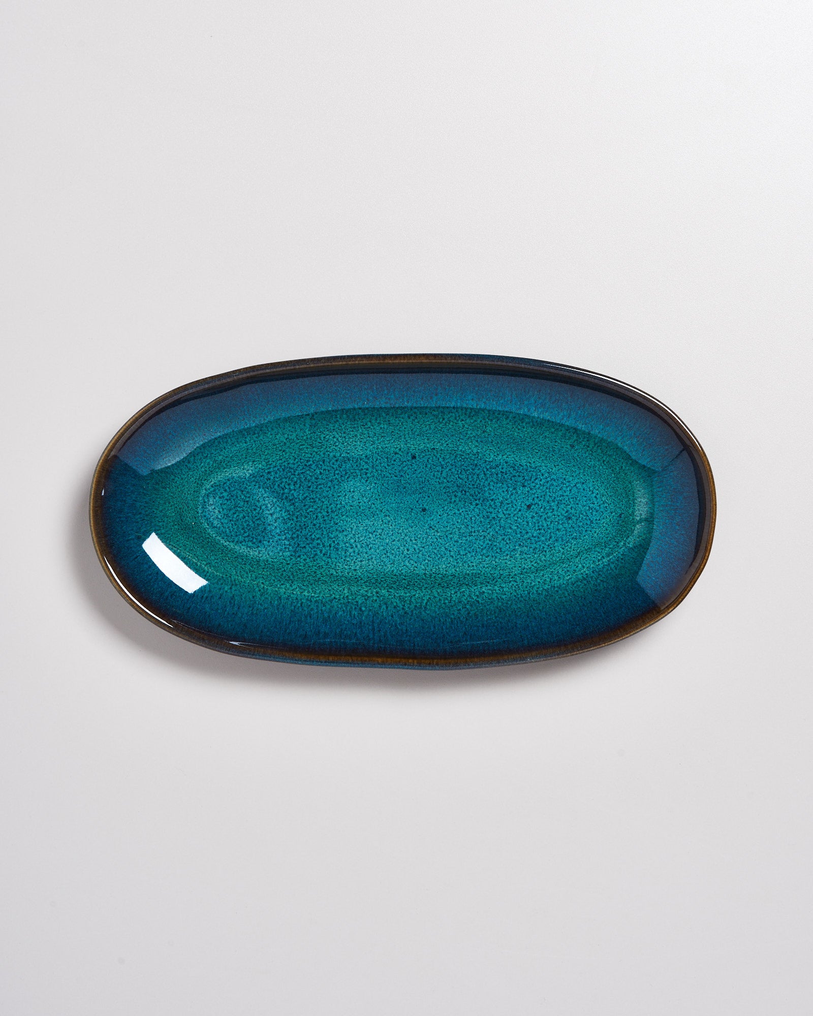 Blau-grüne ovale Keramikplatte auf weißem Hintergrund.