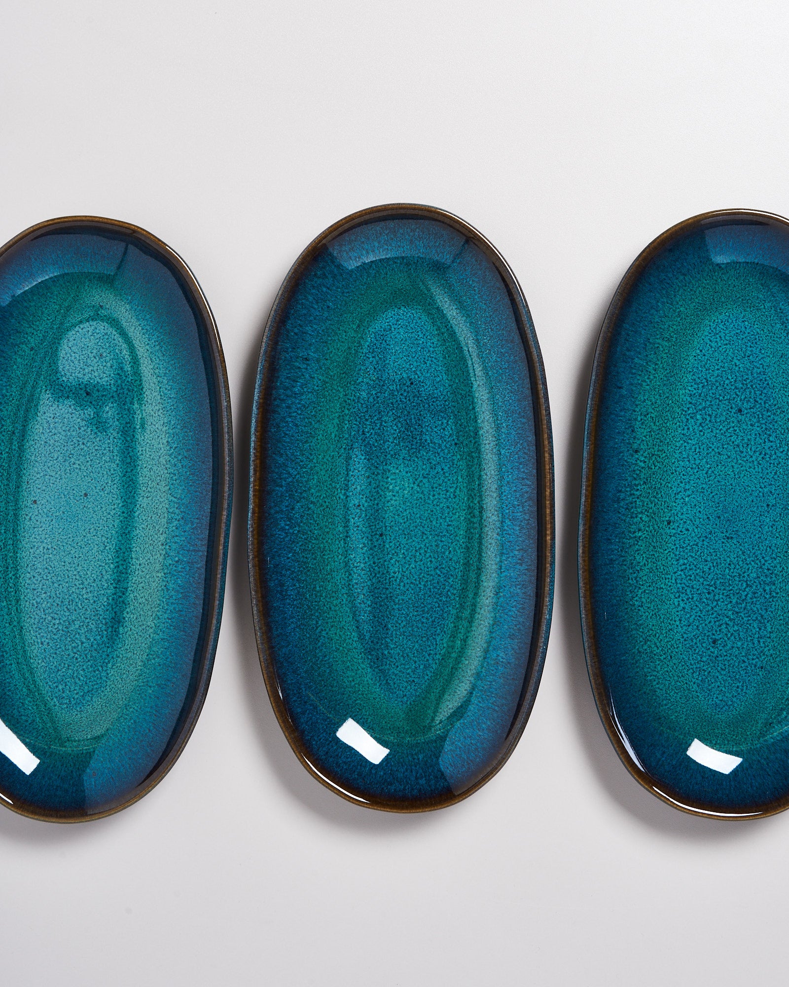 Drei ovale Teller in verschiedenen Blautönen mit glänzender Oberfläche auf weißem Hintergrund.