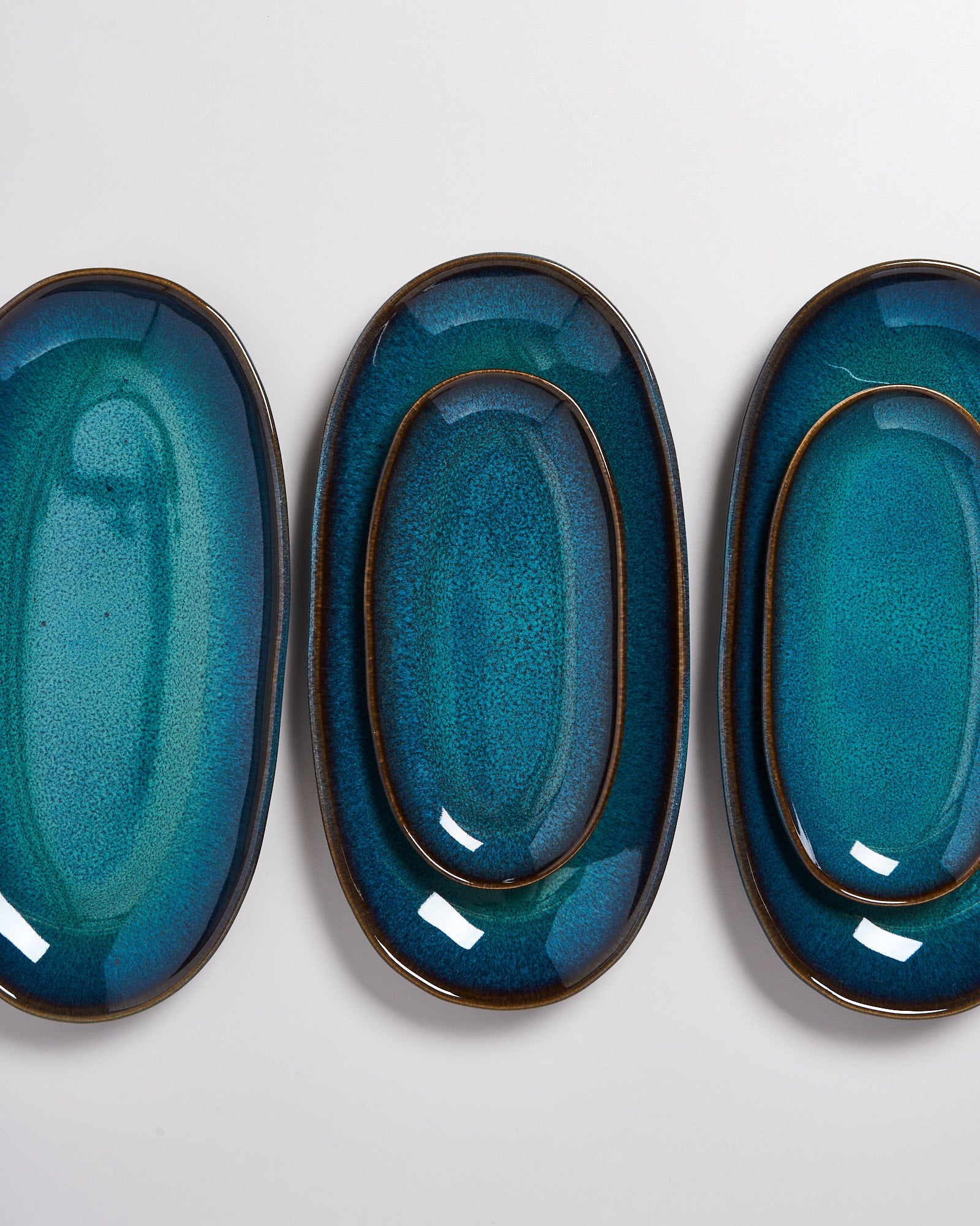 Drei gestapelte, ovalförmige Teller in verschiedenen Blautönen auf einer weißen Oberfläche.
