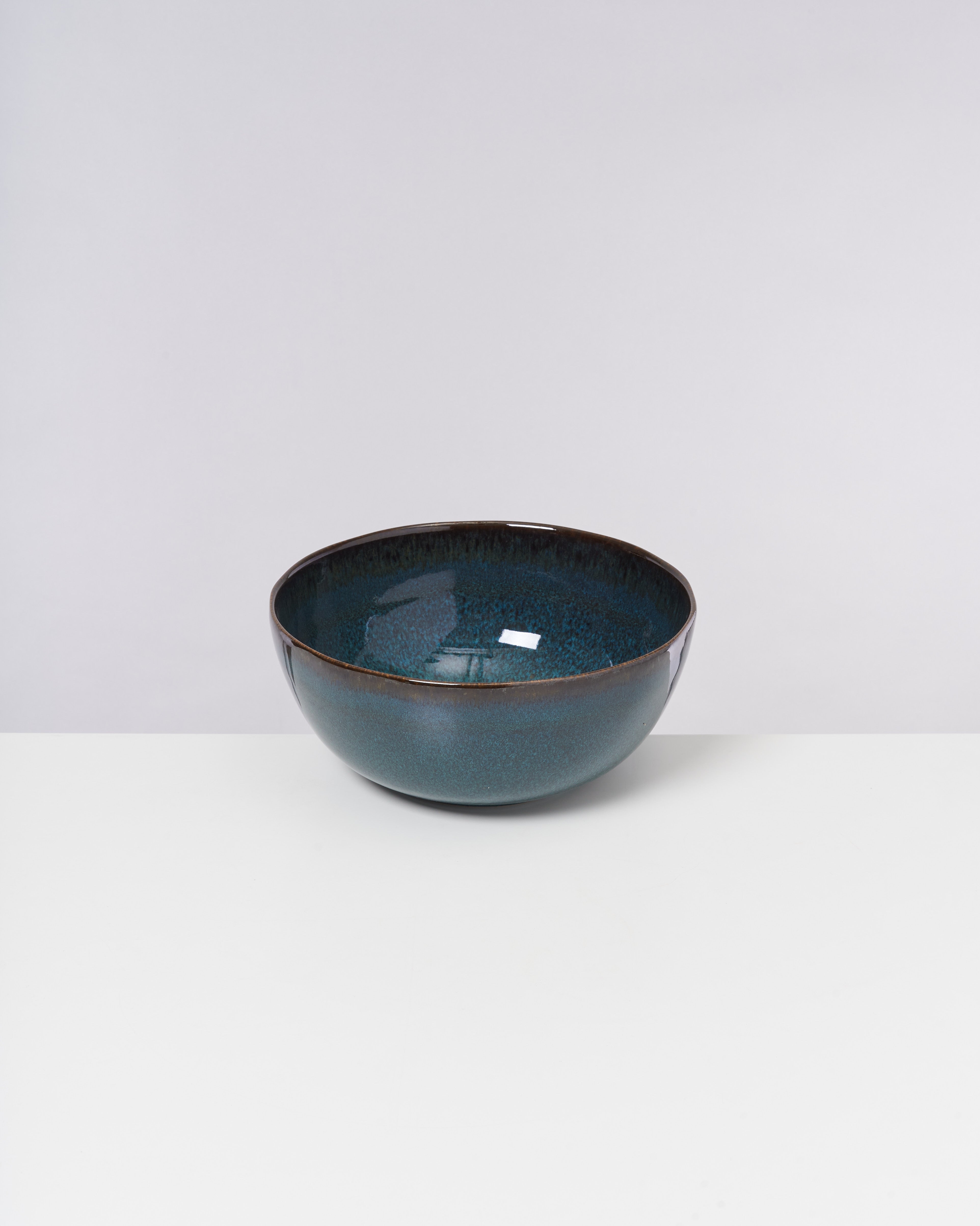 Eine blaue Keramikschüssel mit glänzender Glasur steht auf einer weißen Oberfläche vor einem grauen Hintergrund.