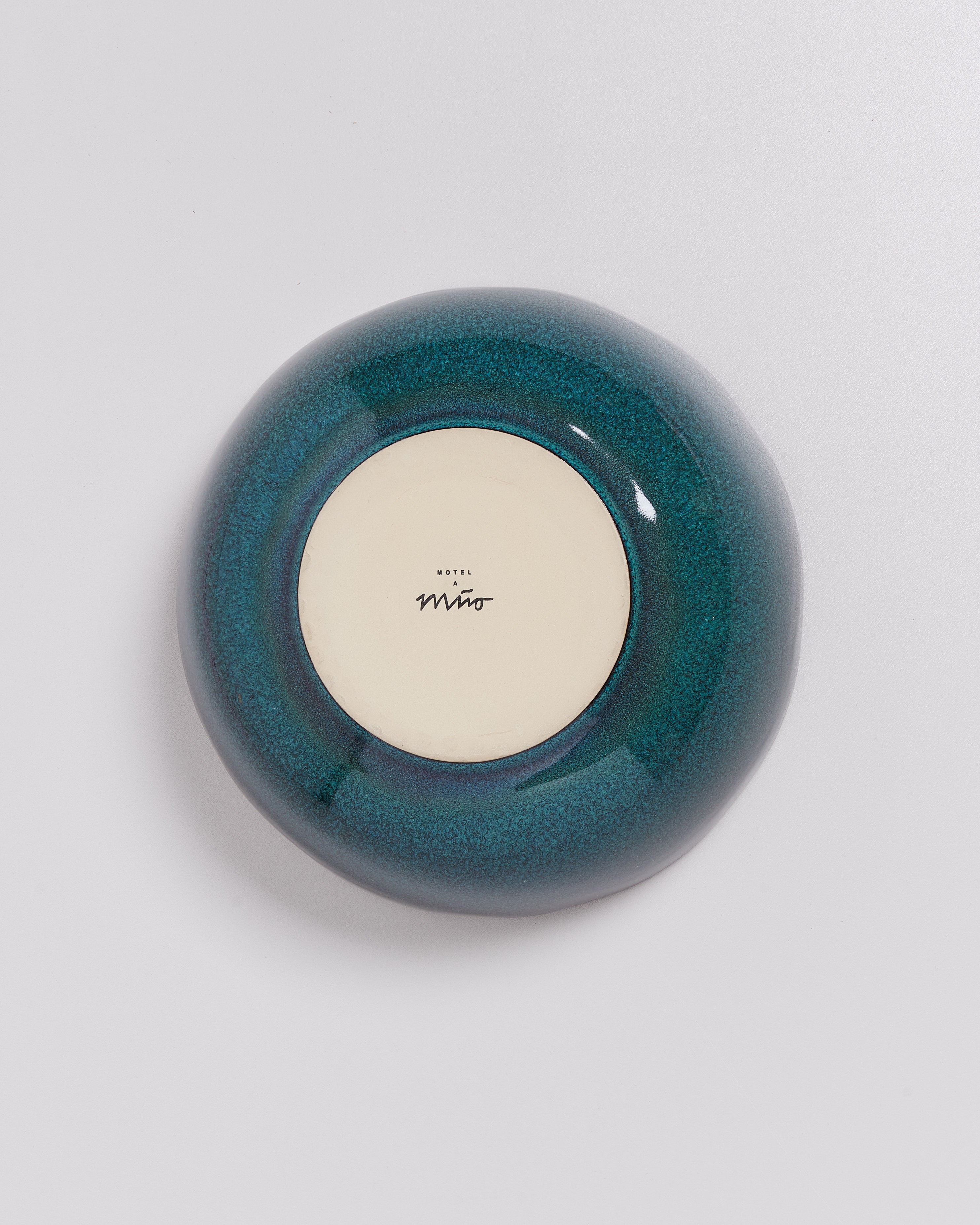 Blaugrüner Teller mit weißem Boden und „Hotel Mino“ Schriftzug, auf hellem Hintergrund.