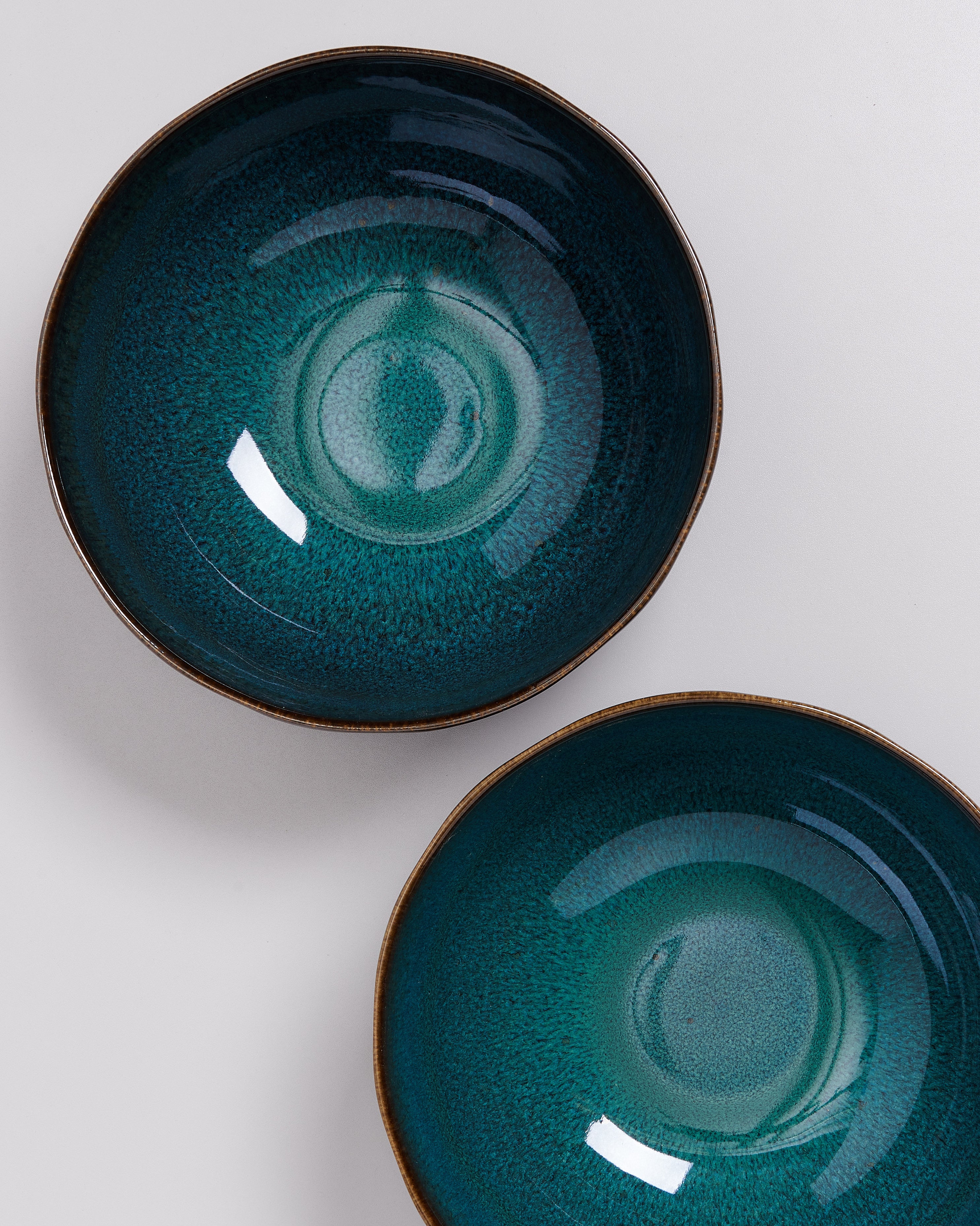 Zwei türkisfarbene, runde Keramikschalen mit glatter glänzender Oberfläche auf hellem Hintergrund.