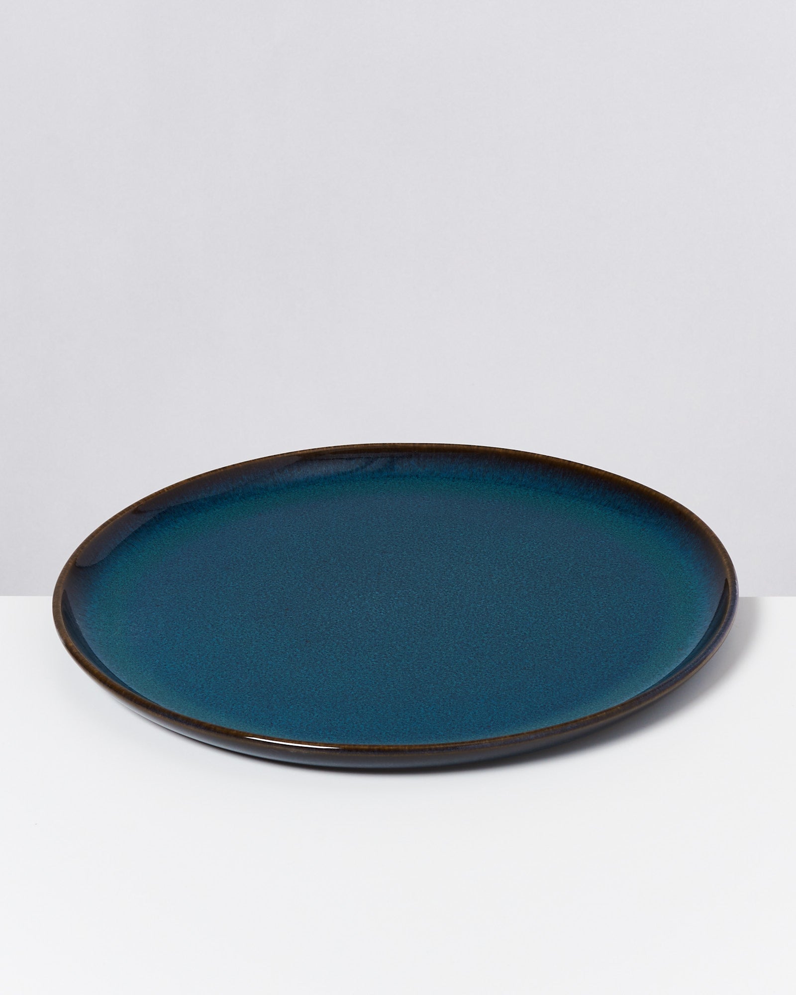 Blauer Teller mit dunklem Rand auf weißem Hintergrund.