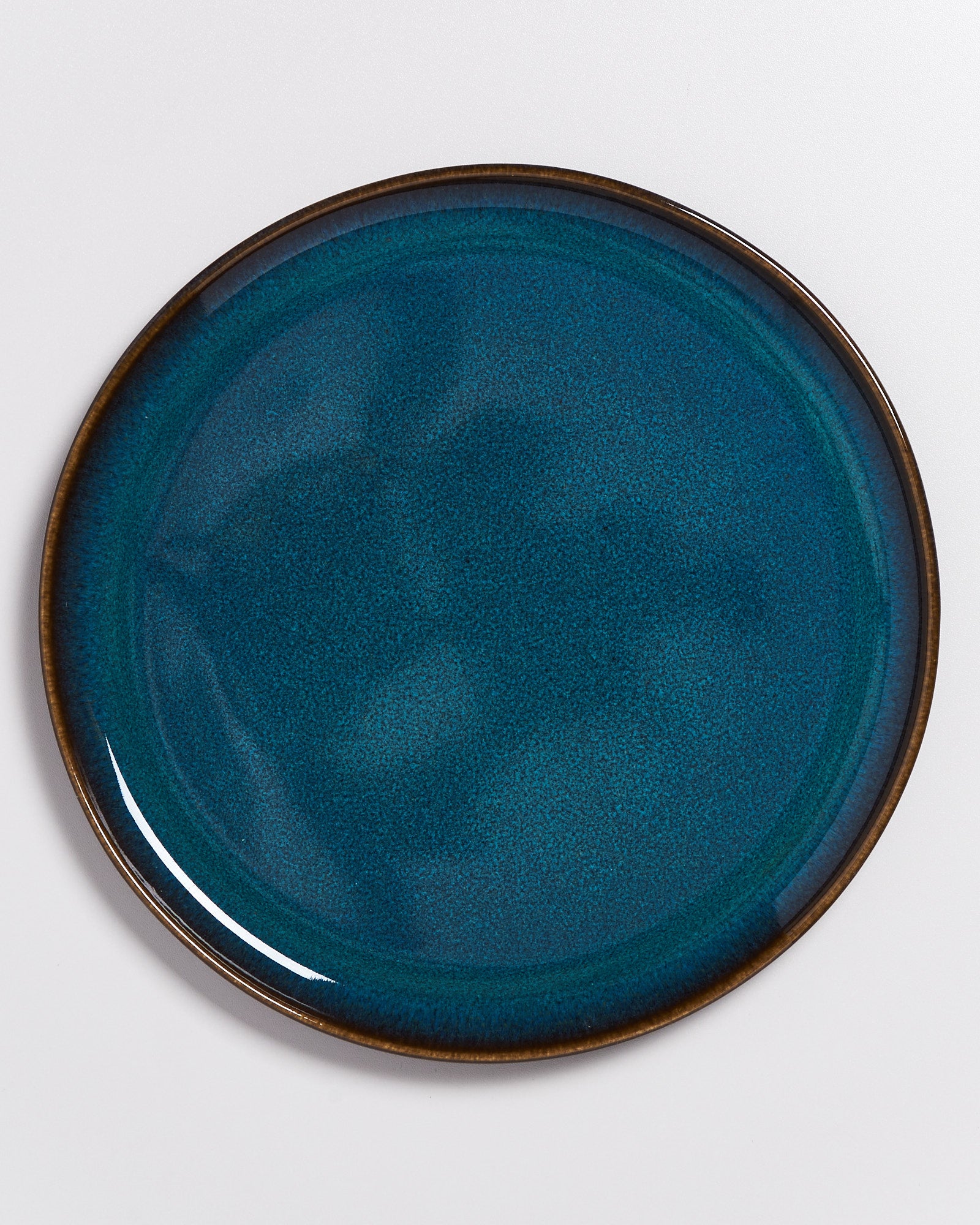 Ein runder, blau glasierten Keramikteller mit dunklem Rand auf weißem Hintergrund.