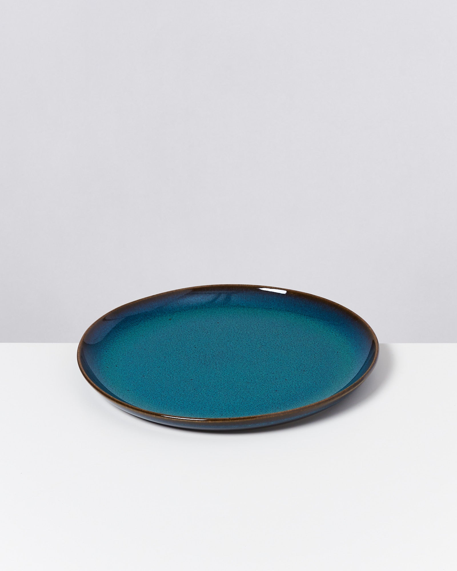 Blauer Keramikteller mit braunem Rand auf weißem Hintergrund.