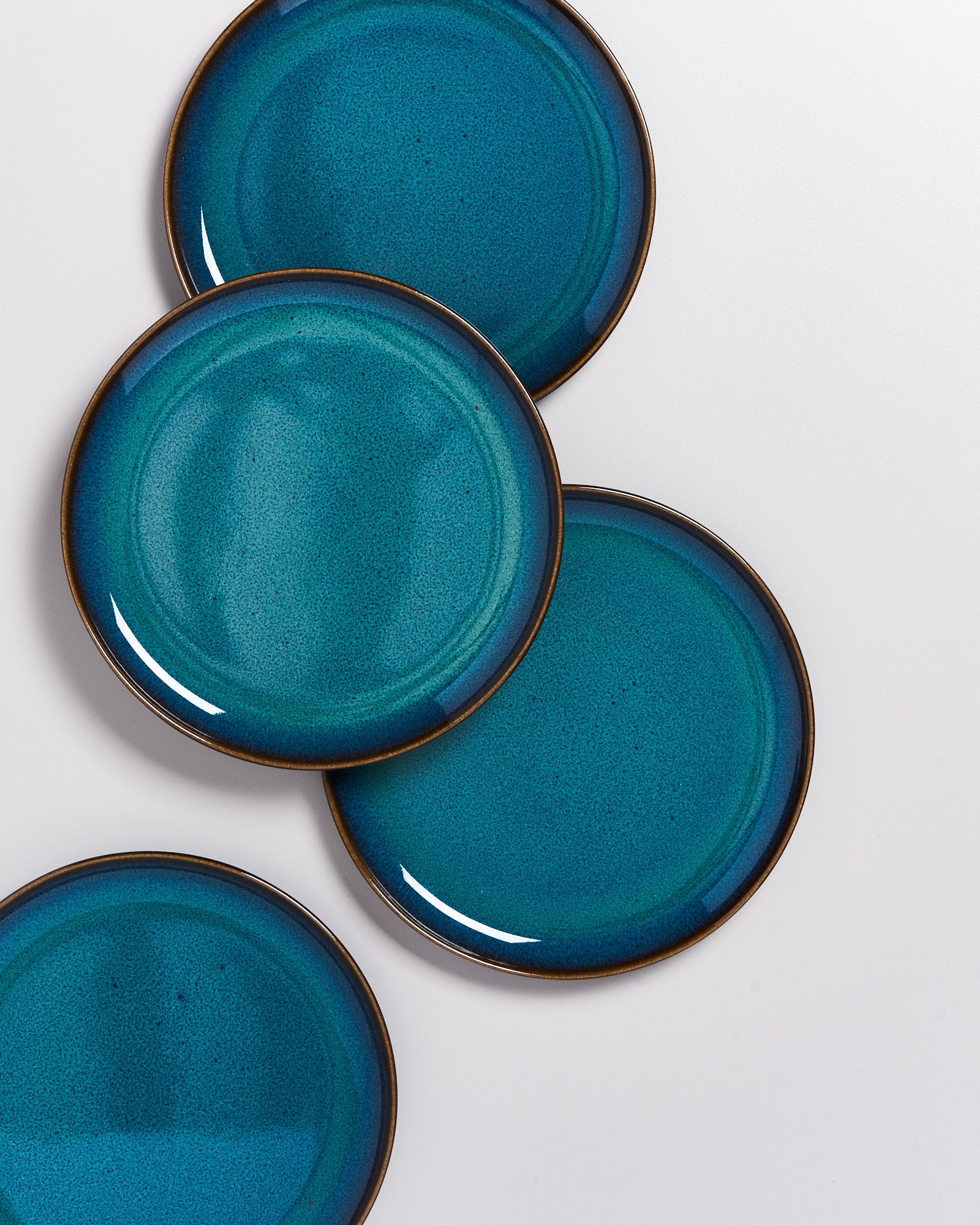 Vier überlappende, türkisfarbene Teller mit einem dunklen Rand auf einem hellen Hintergrund.