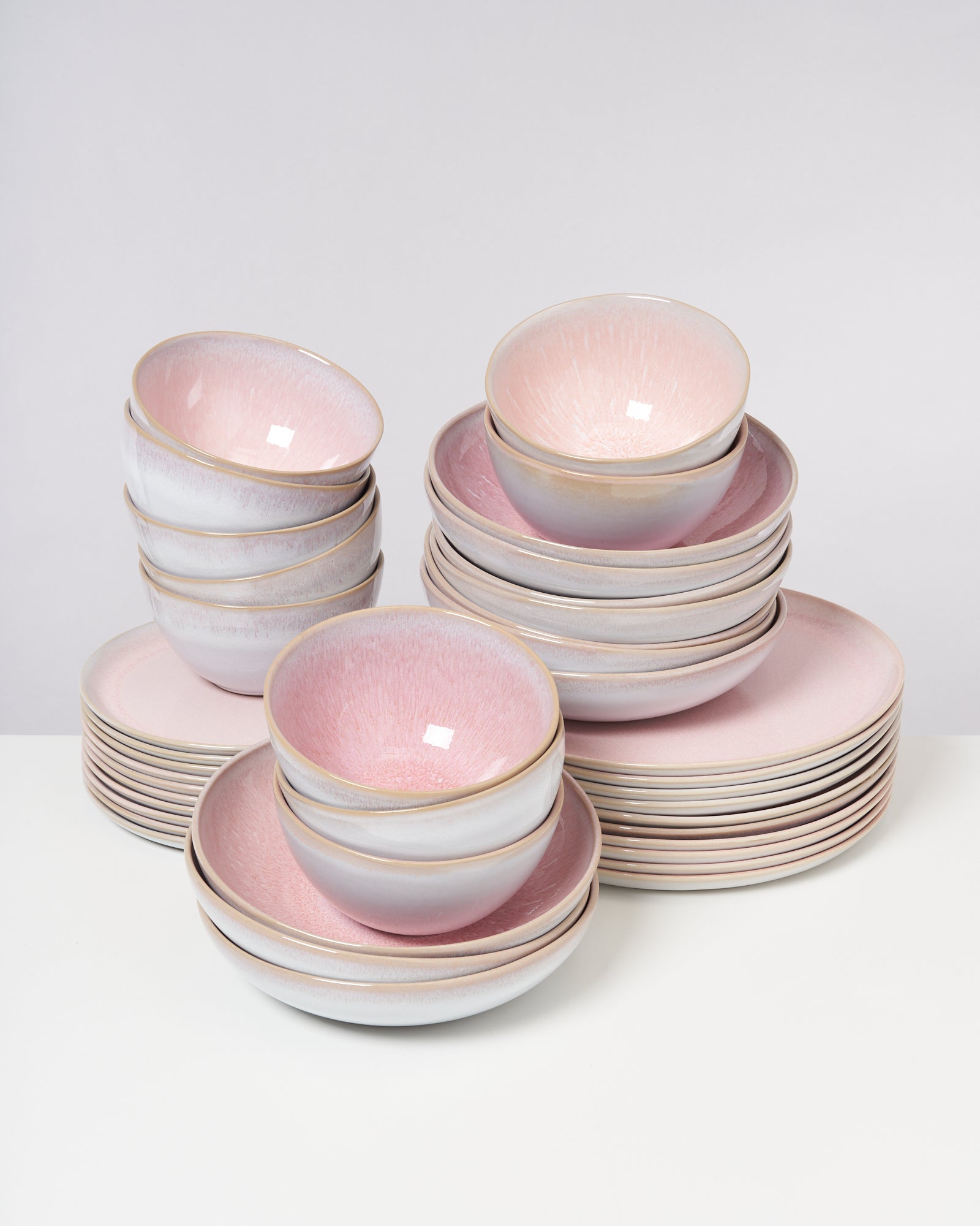 Mehrere gestapelte rosa und weiße Schüsseln und Teller auf einer weißen Oberfläche.
