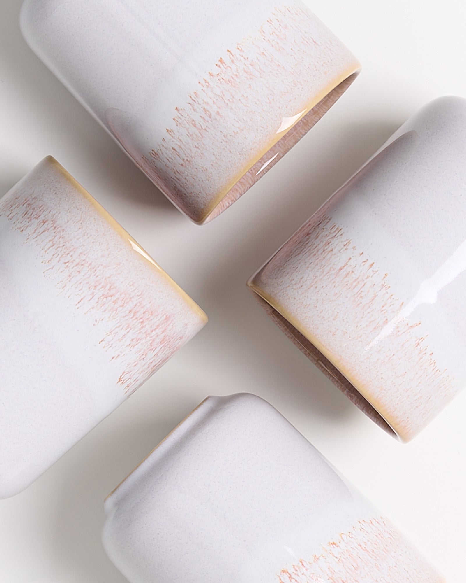 Vier weiße Tassen mit braunen Verfärbungen an den Rändern liegen auf einer weißen Oberfläche.