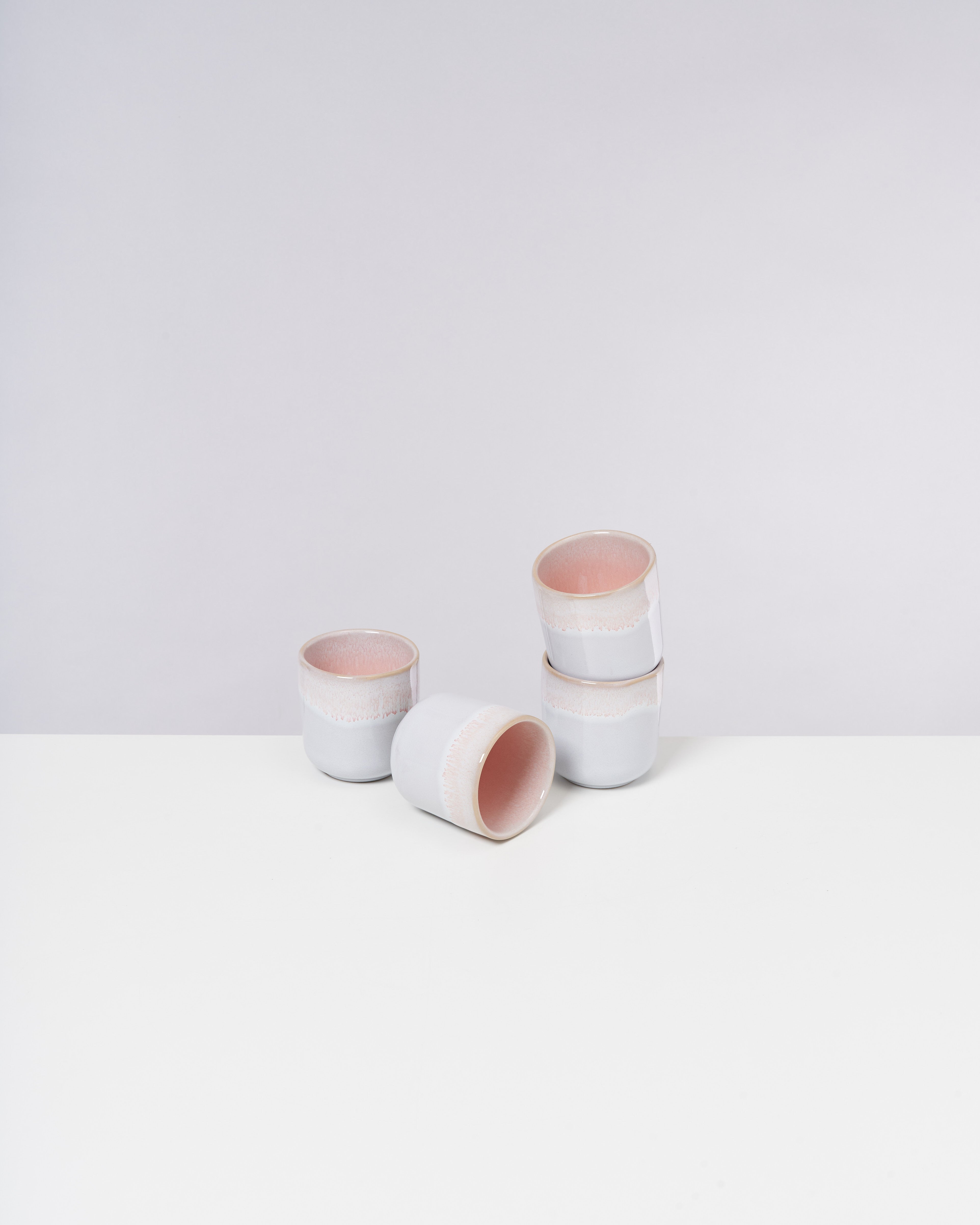 Fünf weiße Keramiktassen mit rosa Innenseite auf einem weißen Tisch, einige gestapelt, andere liegend.