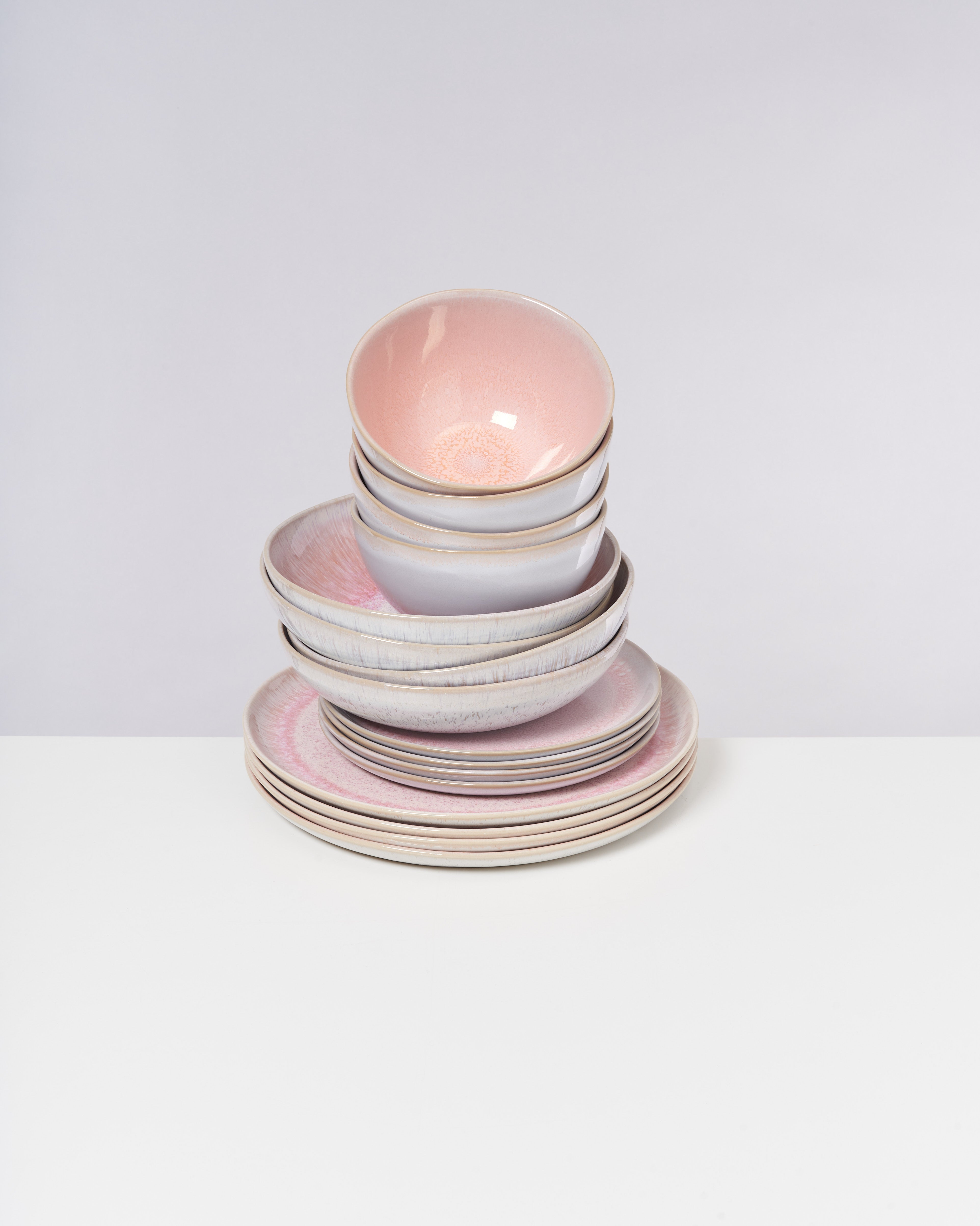 Ein Stapel von rosa Schalen und Tellern steht auf einem weißen Tisch vor einem grauen Hintergrund.