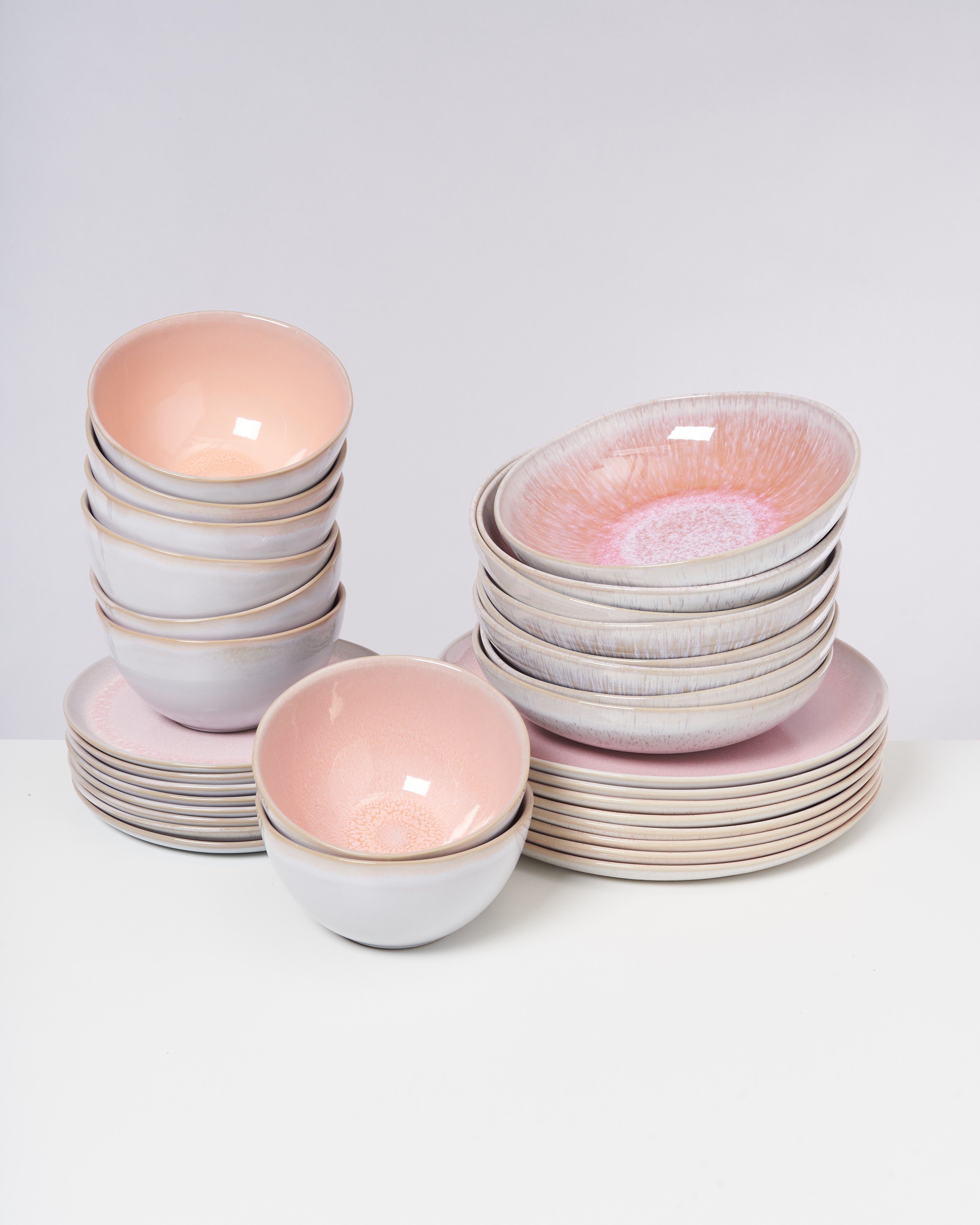 Gestapeltes Geschirrset aus mehreren Schüsseln und Tellern in Pastellfarben auf einer weißen Oberfläche.
