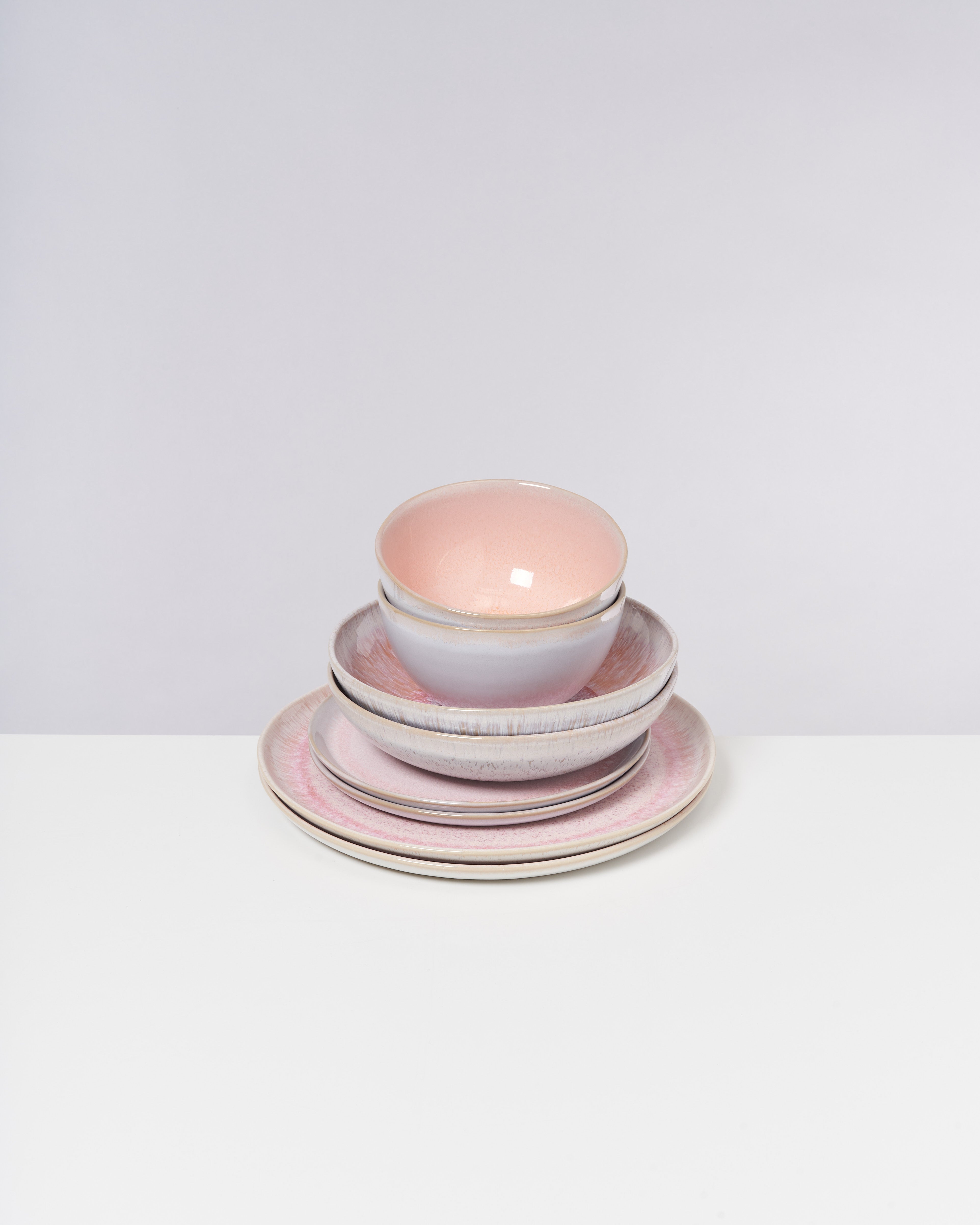 Ein Stapel aus Porzellangeschirr mit einem rosa Schälchen, Tellern und einer Schüssel auf weißem Hintergrund.
