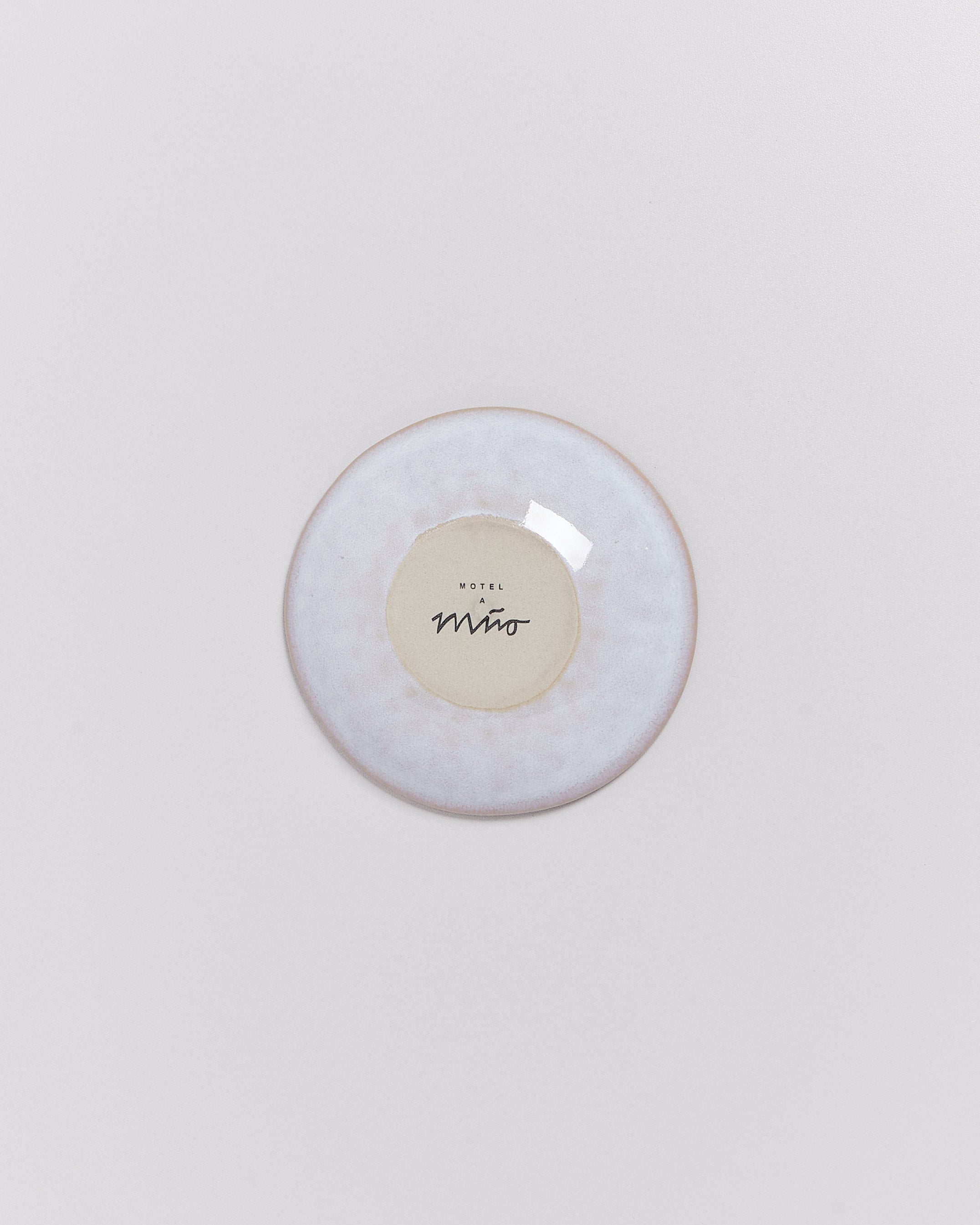 Eine runde, glatte Untertasse mit einem beige-grauen Rand und einem Logo in der Mitte, auf weißem Hintergrund.
