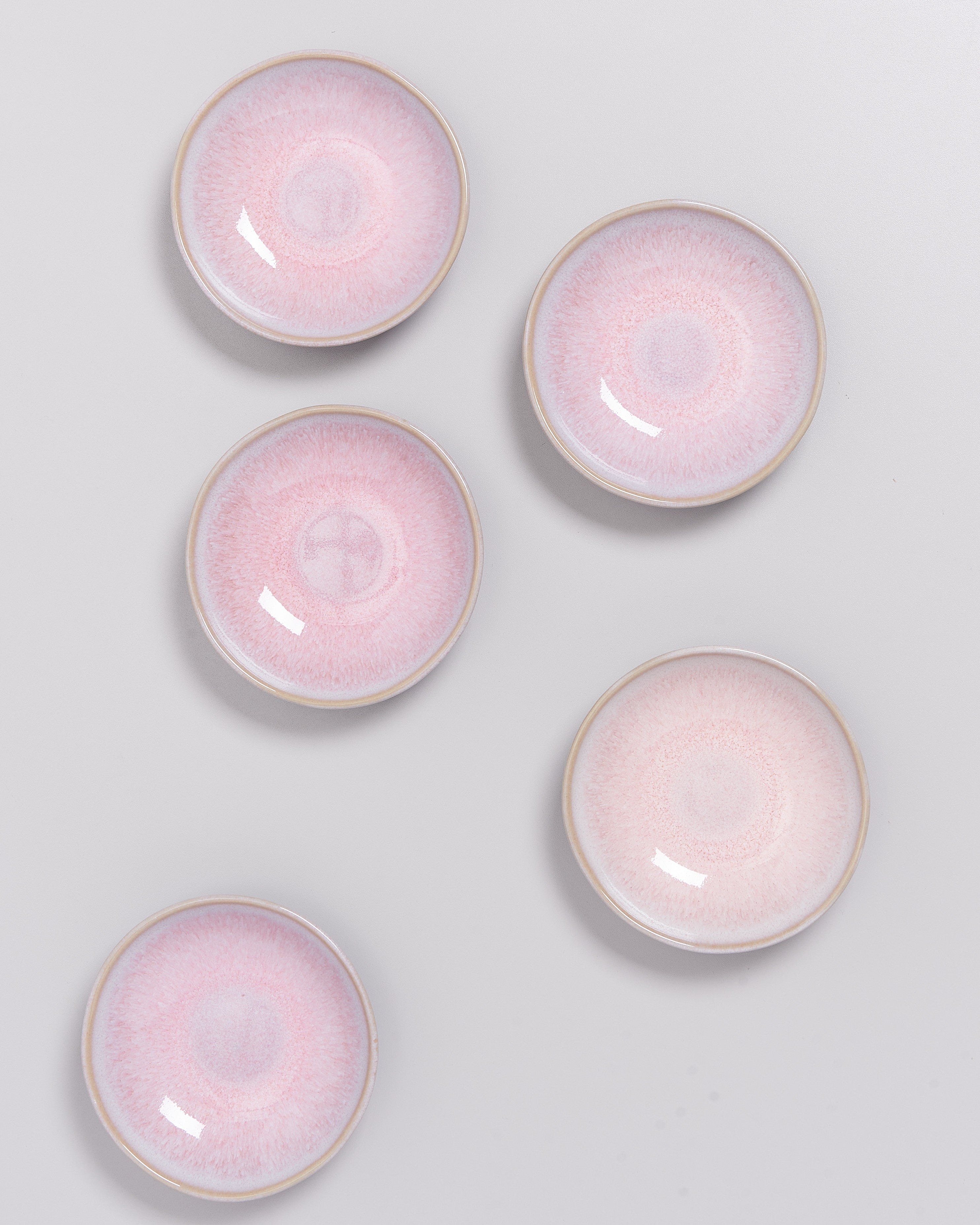 Fünf rosa Keramikteller auf einer grauen Oberfläche angeordnet.