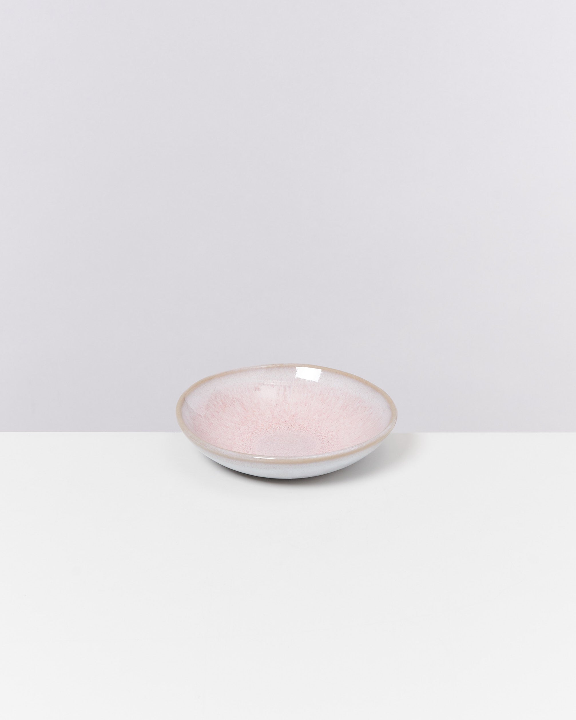 Eine rosa Schale mit mattem Finish steht auf einem weißen Tisch vor einem grauen Hintergrund.