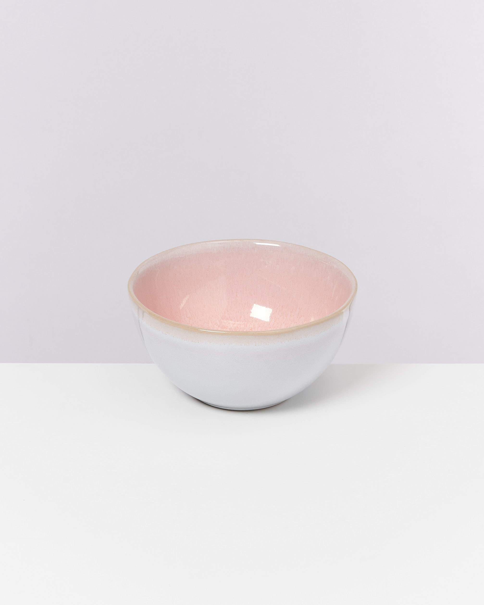 Eine Keramikschüssel mit rosa Innen- und grauer Außenseite steht auf einem weißen Tisch vor einem hellgrauen Hintergrund.
