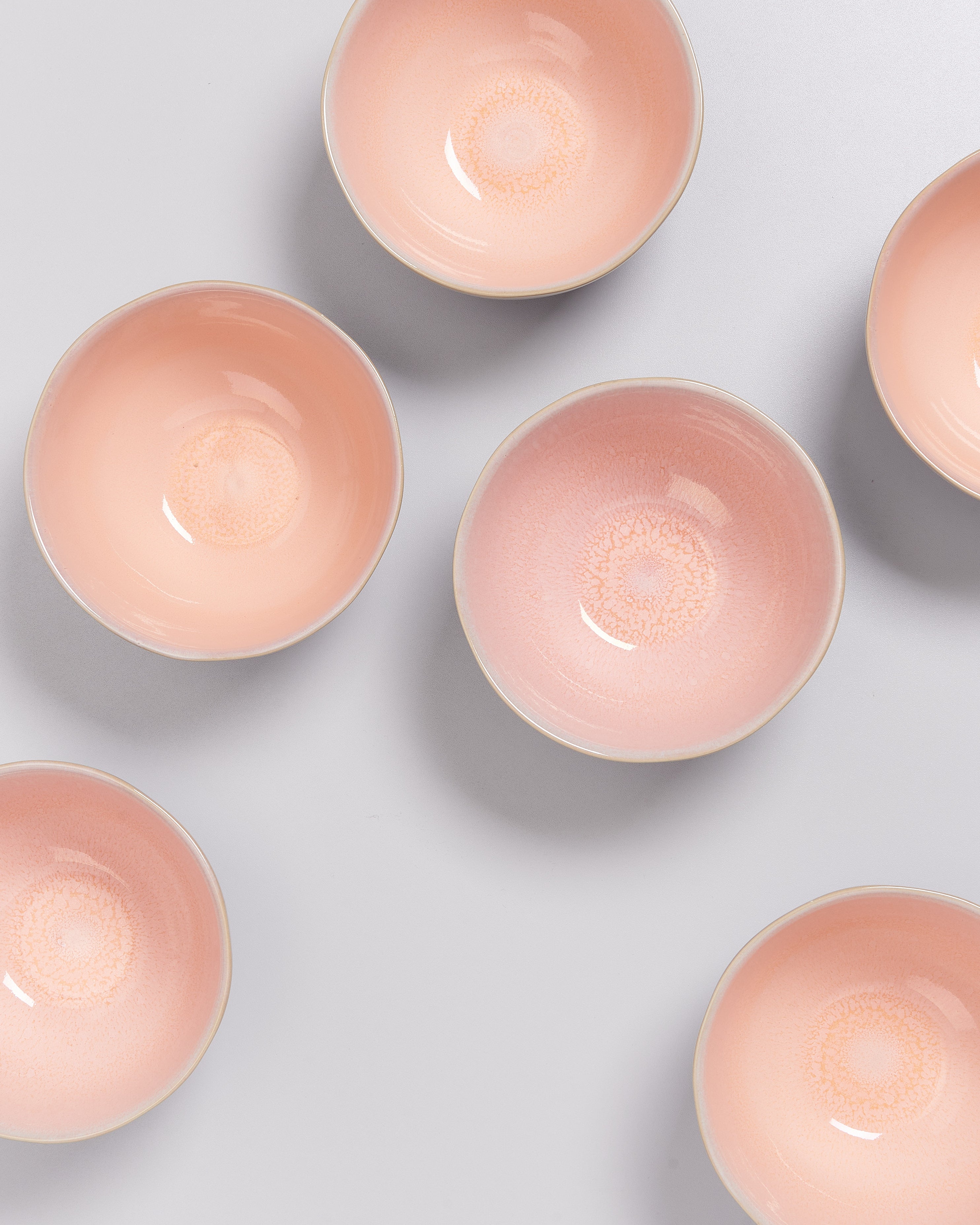Sechs rosafarbene Schalen auf einem hellgrauen Hintergrund in einer diagonalen Anordnung.