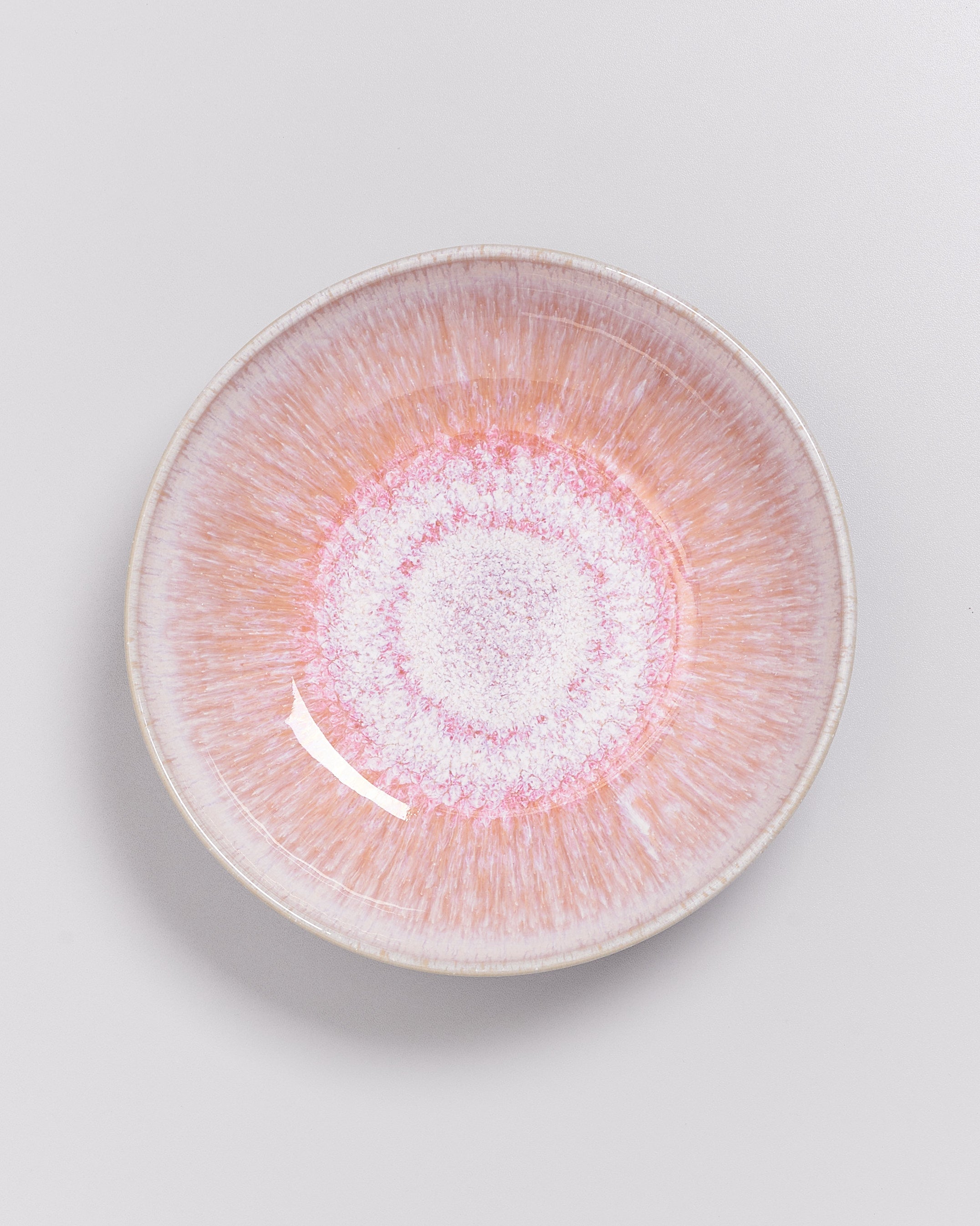 Runder, pastellfarbener Teller mit radialem Muster in Rosa und Weiß, auf grauem Hintergrund fotografiert.