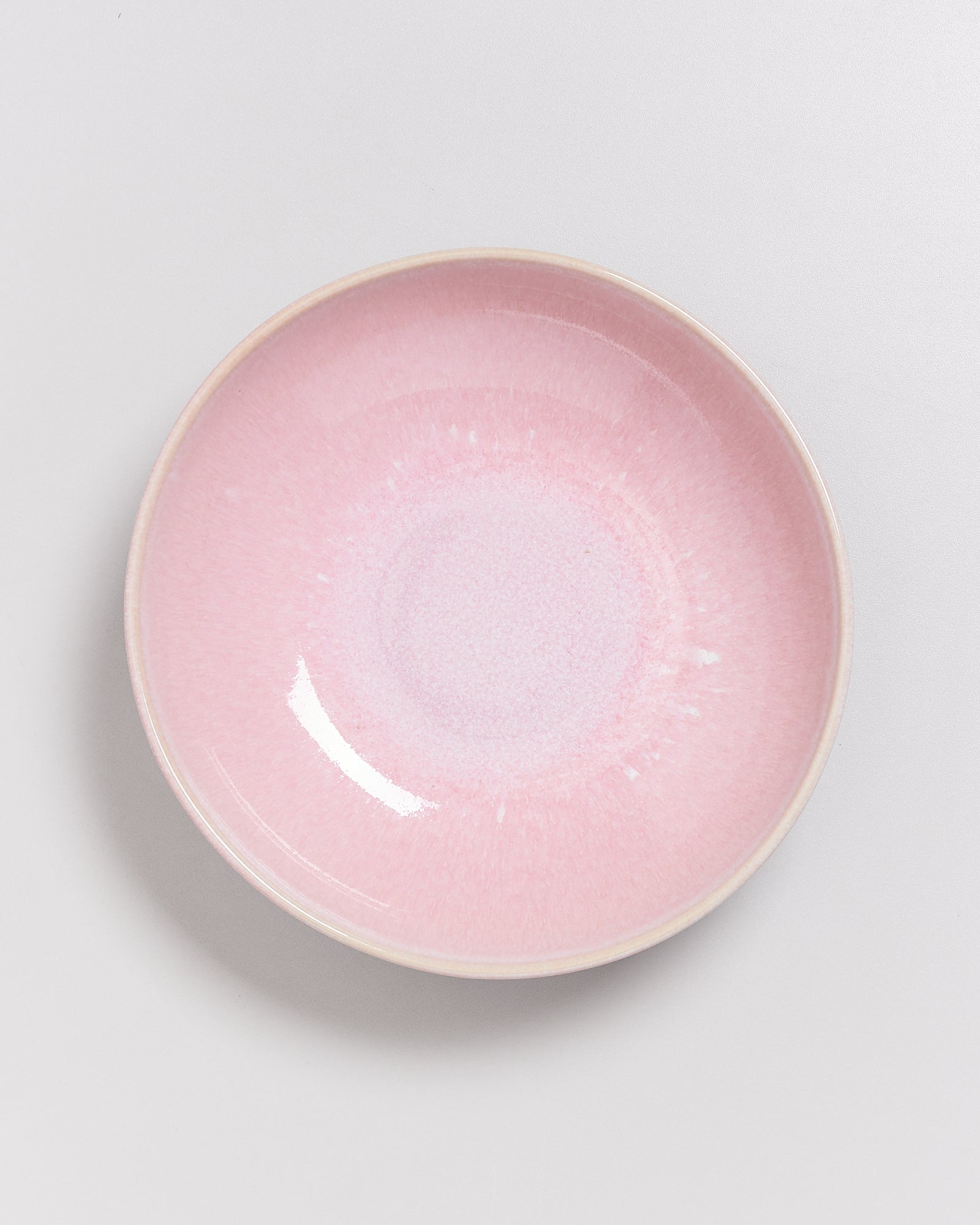 Rosa Keramikschüssel mit blassweißen Verläufen auf einem grauen Hintergrund.