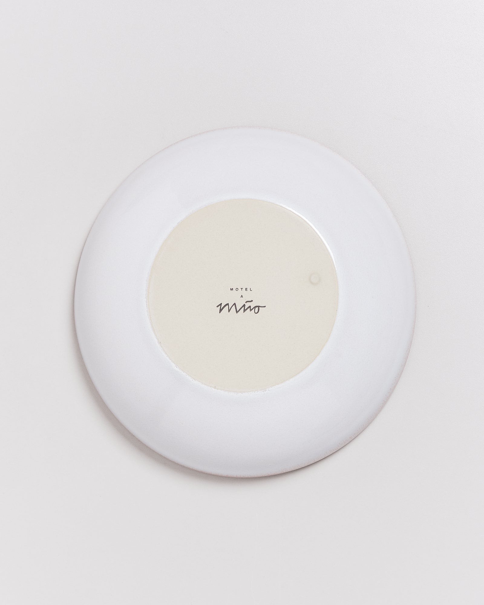 Weiße, runde Platte mit dem Schriftzug "Motel a Miro" in der Mitte, auf hellem Hintergrund.