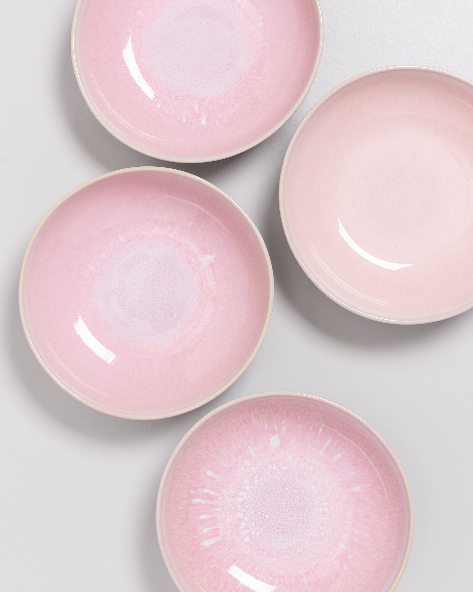Vier rosa Keramikteller mit weißem Verlauf auf hellem Hintergrund angeordnet.