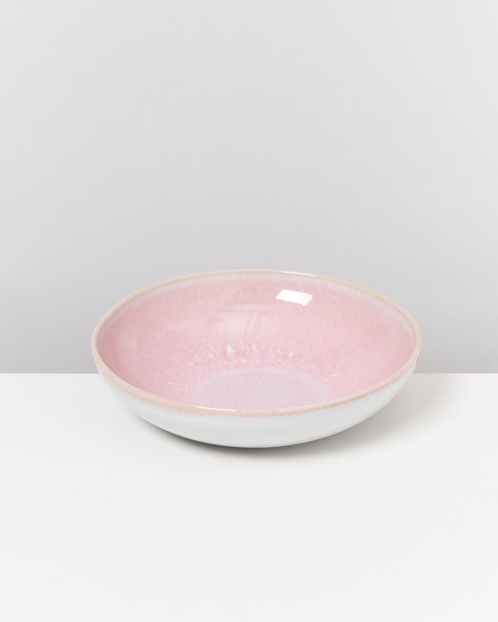 Rosafarbene Keramikschale mit weißem Rand auf weißem Hintergrund.