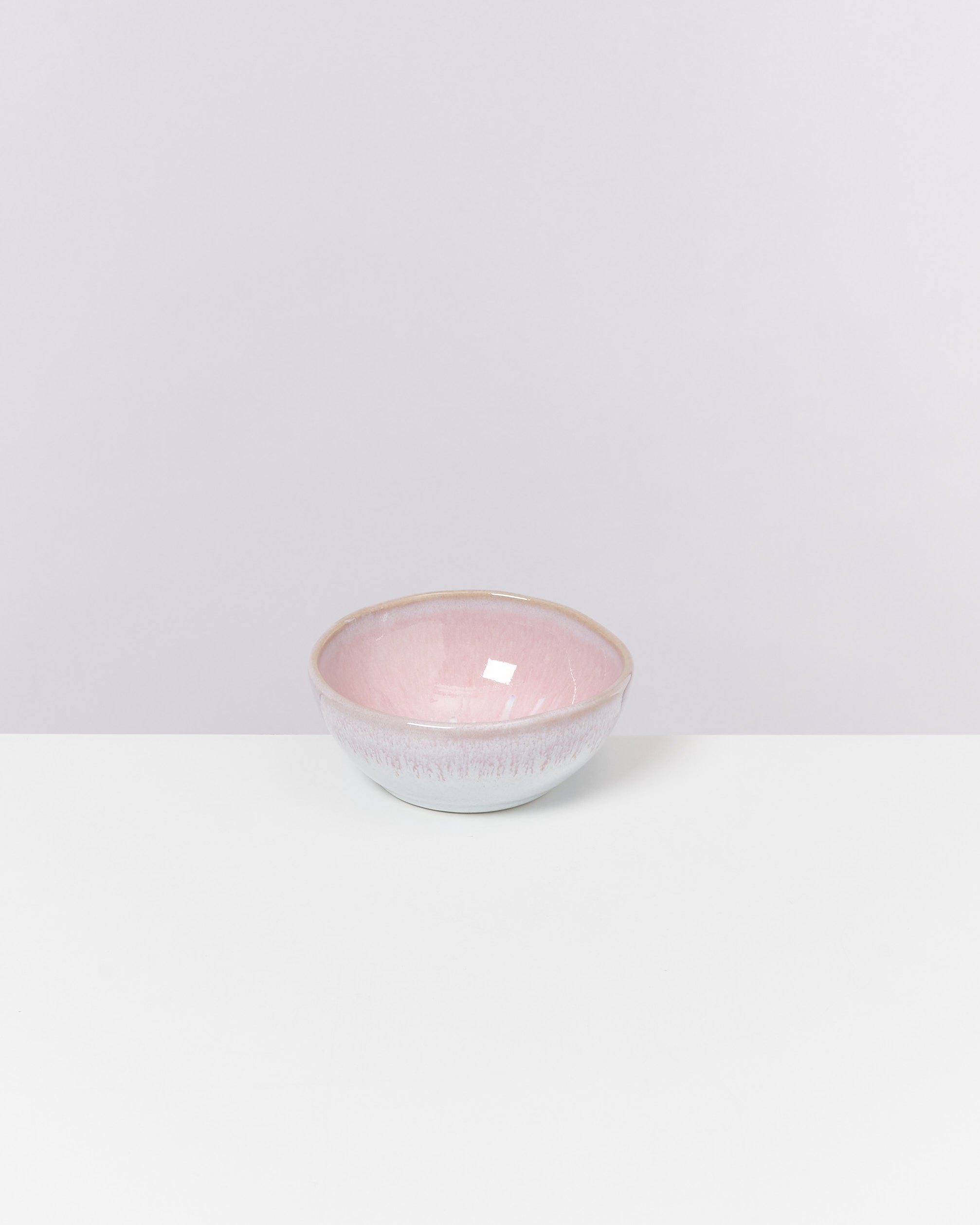 Kleine, rosa- und weißglasierte Schale auf einem weißen Tisch vor einem hellen Hintergrund.
