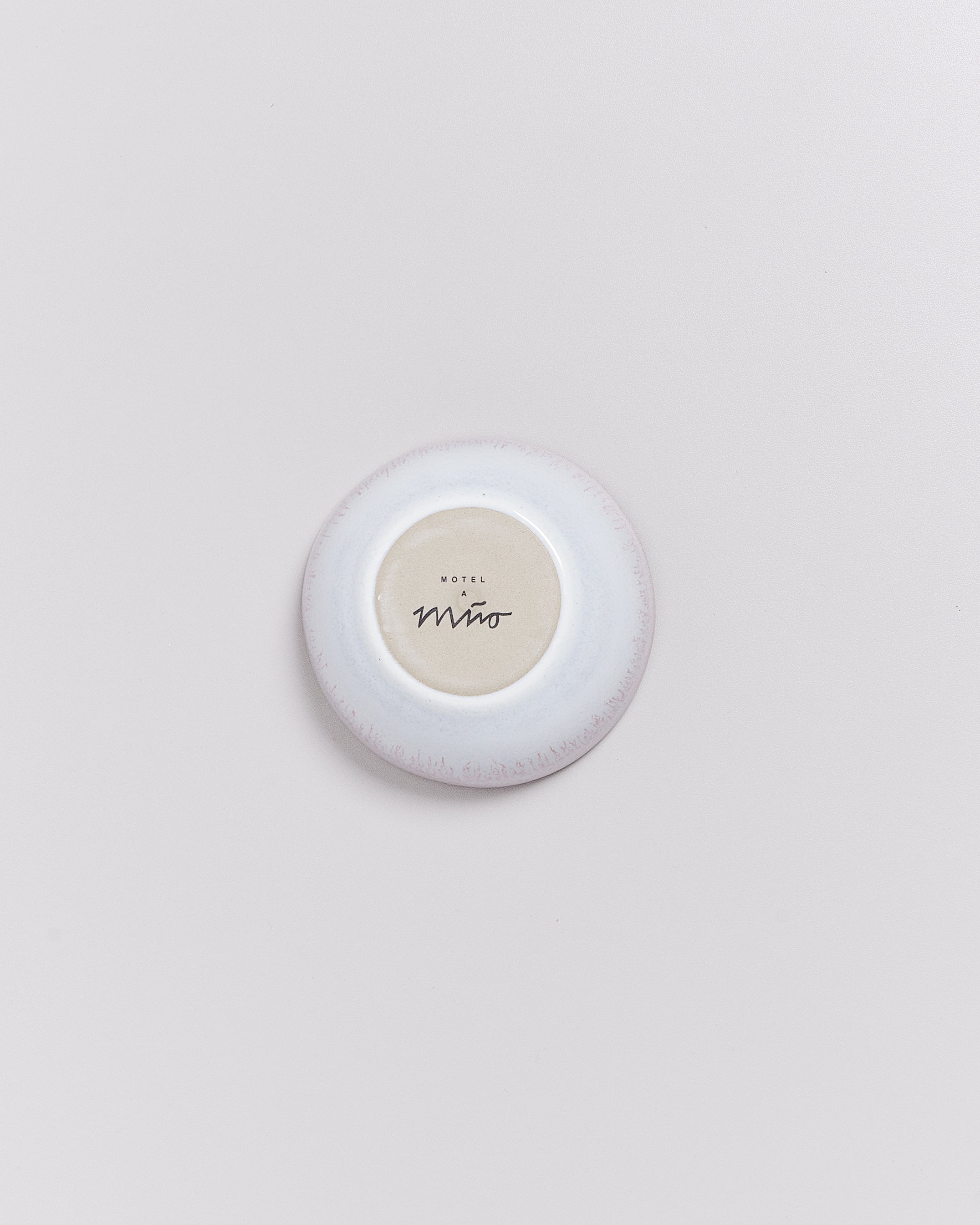 Ein kleiner, runder Teller mit beigem Zentrum und weißem Rand liegt auf einer hellgrauen Oberfläche.