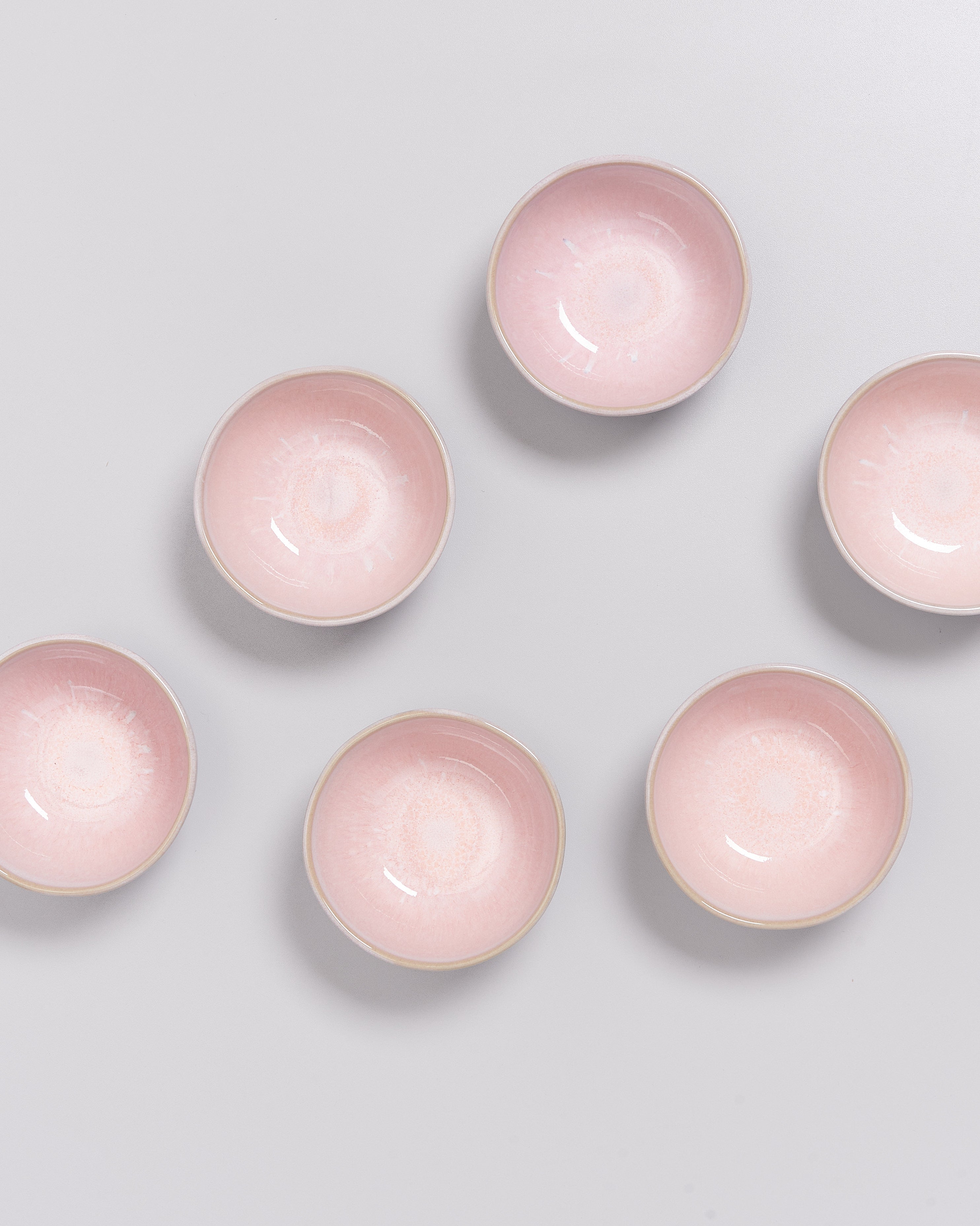 Sechs rosa Schalen sind gleichmäßig auf einer hellgrauen Oberfläche angeordnet.