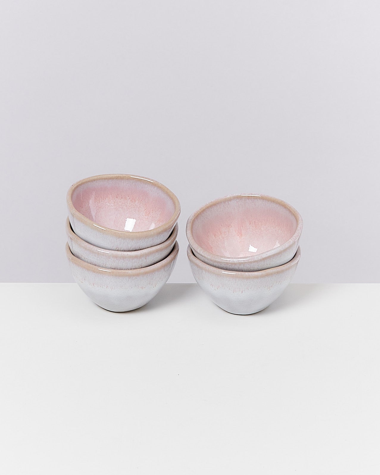 Vier übereinander gestapelte, pastellfarbene Schalen mit rosa Innenseite auf einem weißen Tisch vor grauem Hintergrund.