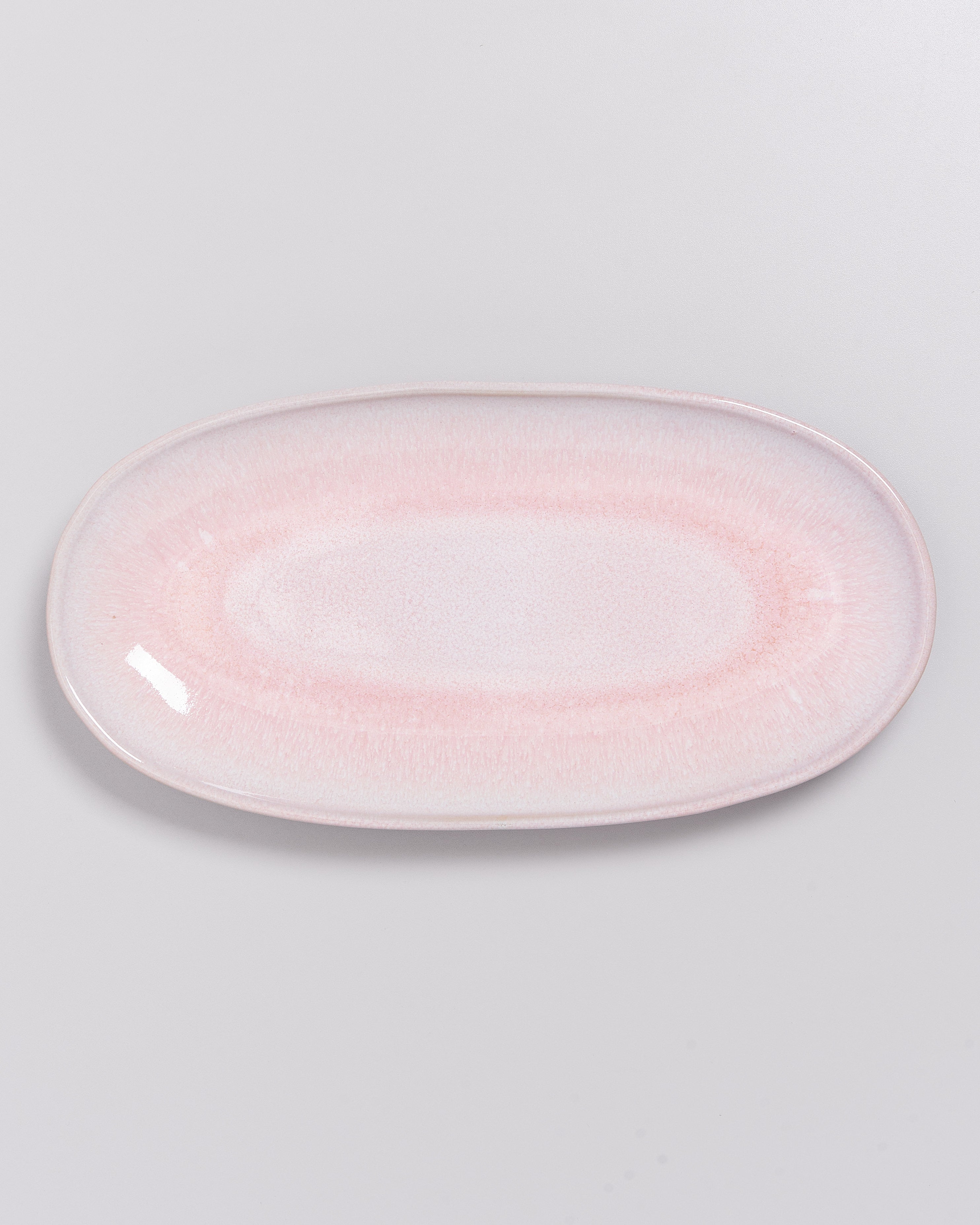 Ein ovaler Teller in zartem Rosa mit glatter Oberfläche auf einem weißen Hintergrund.