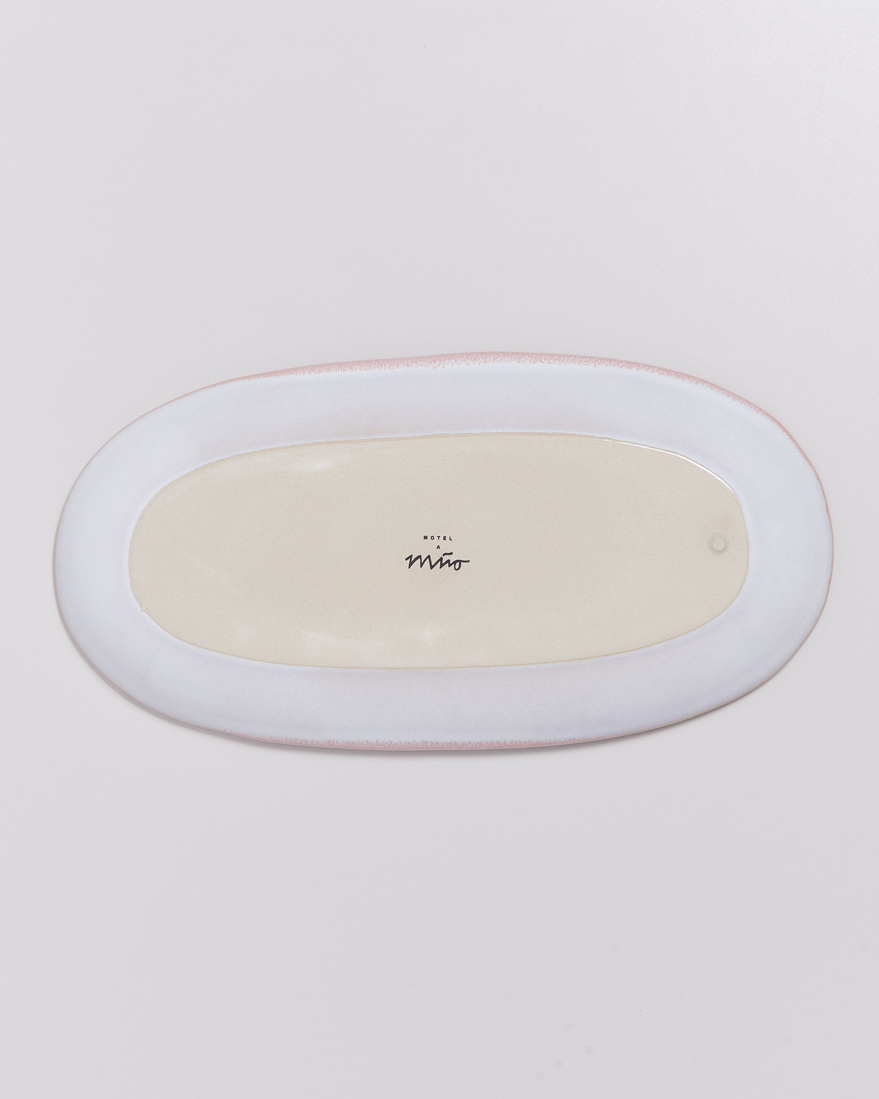 Ovaler Teller mit cremefarbener Innenseite und weißem Rand auf hellem Hintergrund, mit kleiner Aufschrift in der Mitte.