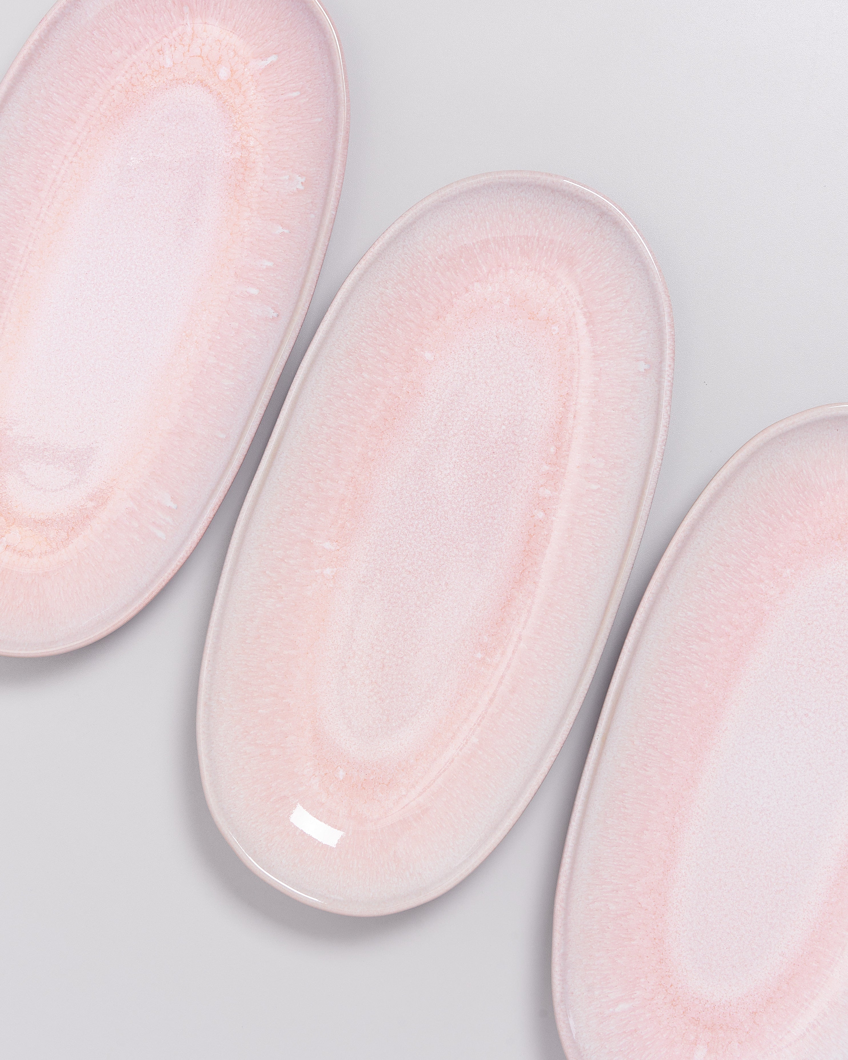 Drei ovale, rosa Teller mit zartem Muster liegen auf einer grauen Oberfläche.
