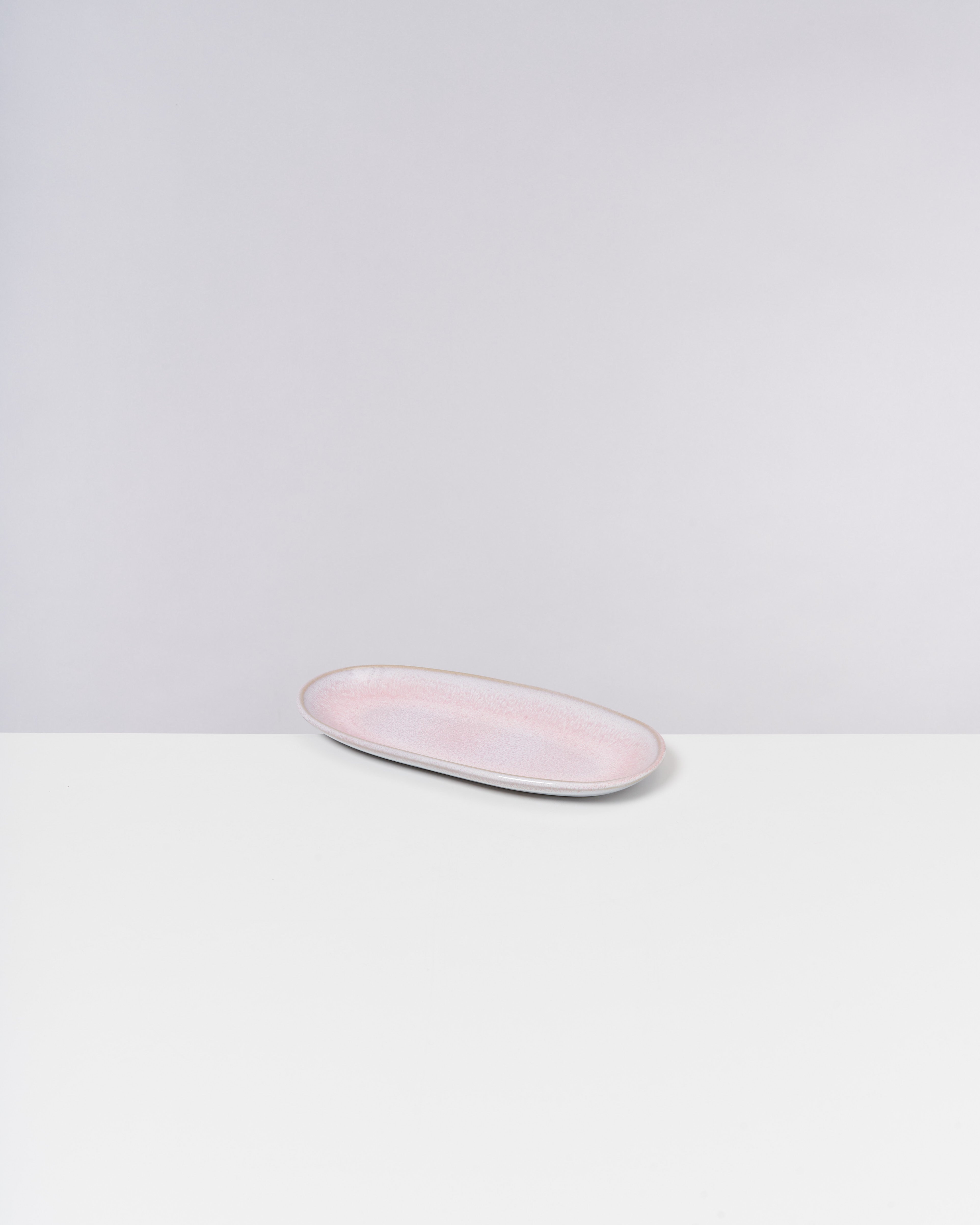 Rosa, ovaler Teller auf einer weißen Oberfläche vor einem grauen Hintergrund.