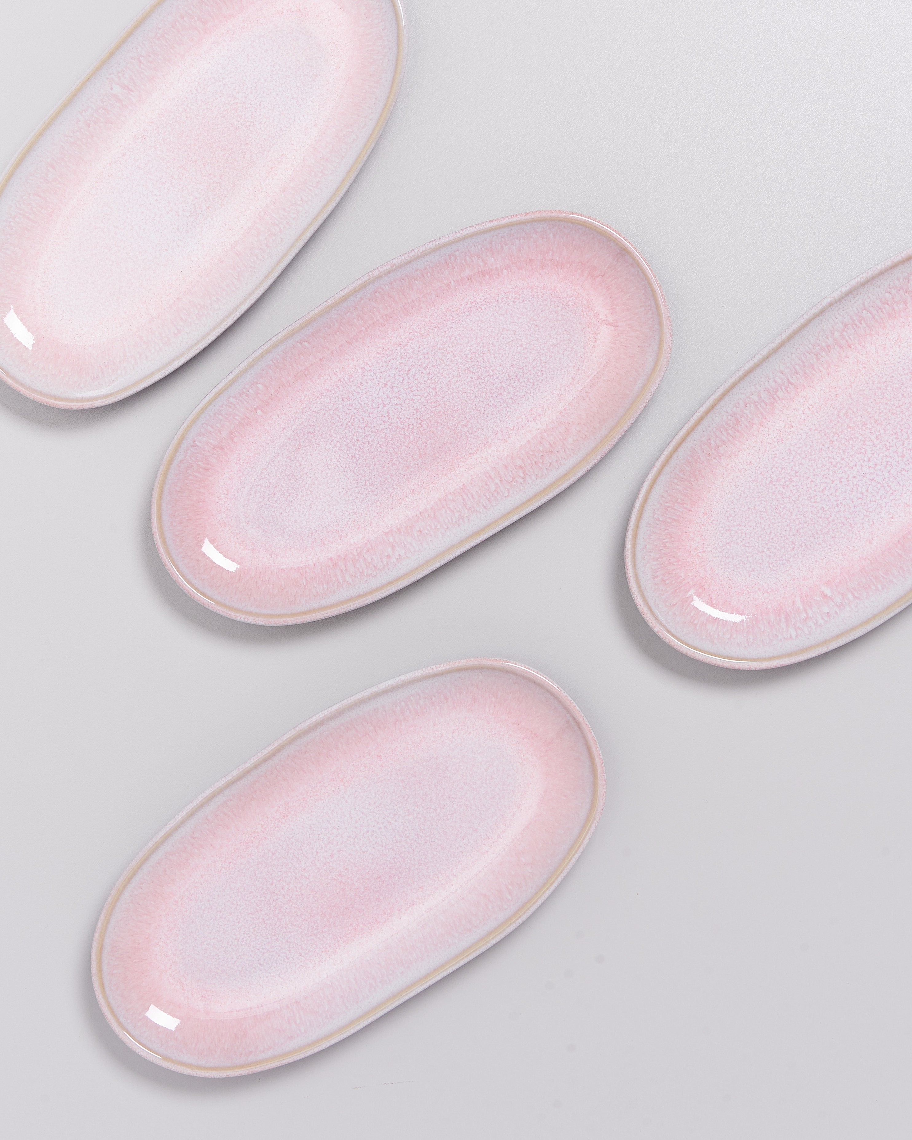 Vier ovale, rosafarbene Keramikteller auf einem hellgrauen Hintergrund angeordnet.