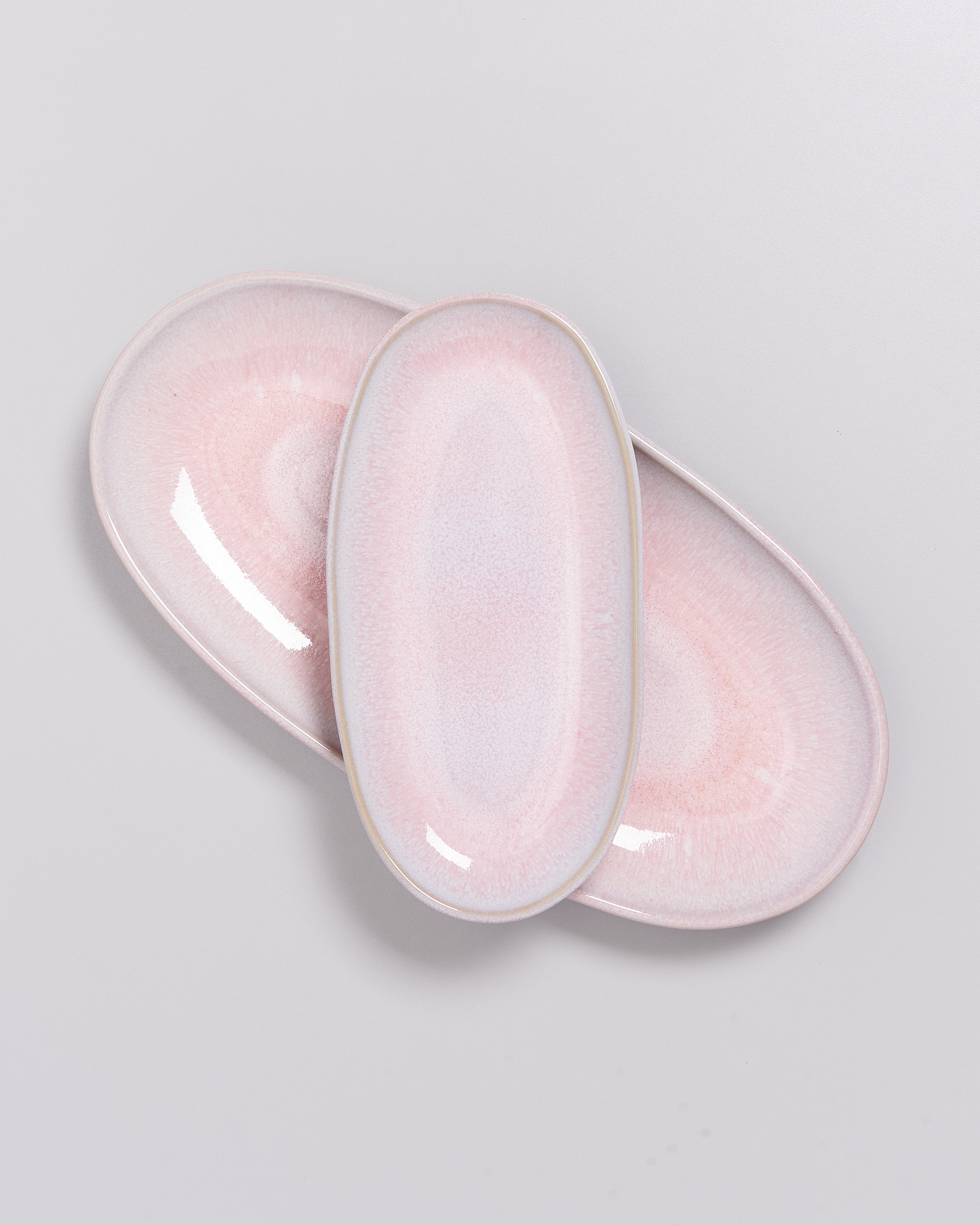Drei ovale, hellrosa Teller mit glatter Oberfläche, die leicht überlappen, auf einem hellgrauen Hintergrund.