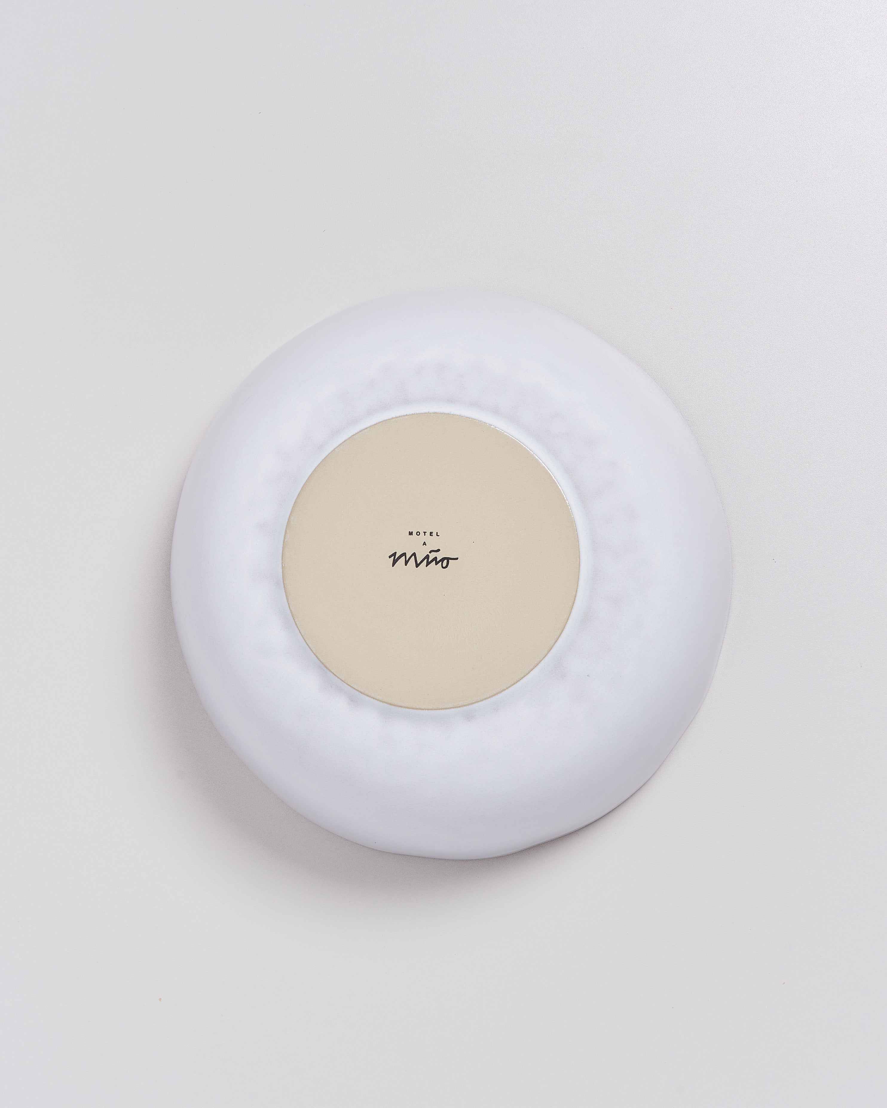 Unterseite eines runden weißen Objekts mit einem beigen Kreis und schwarzer Aufschrift in der Mitte.
