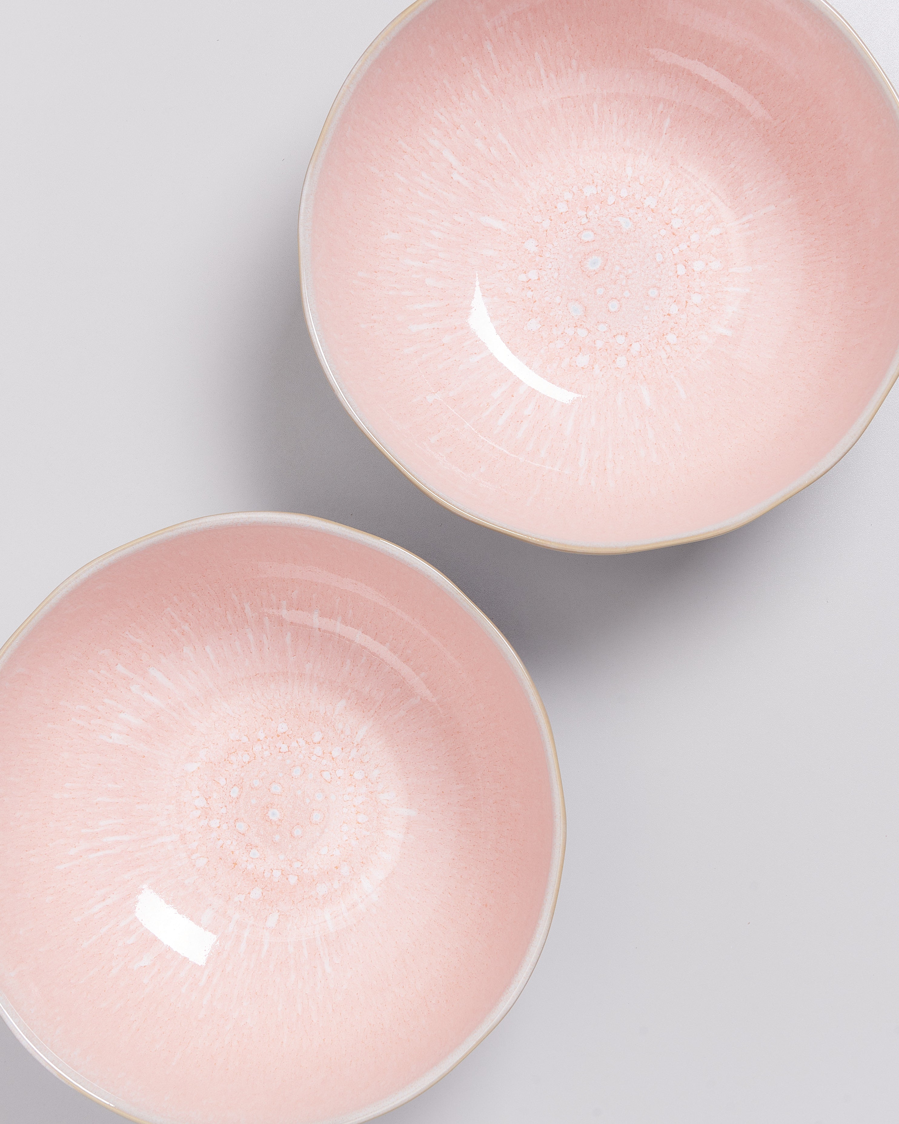 Zwei rosa Schüsseln mit einem dekorativen inneren Muster auf einem hellen Hintergrund.