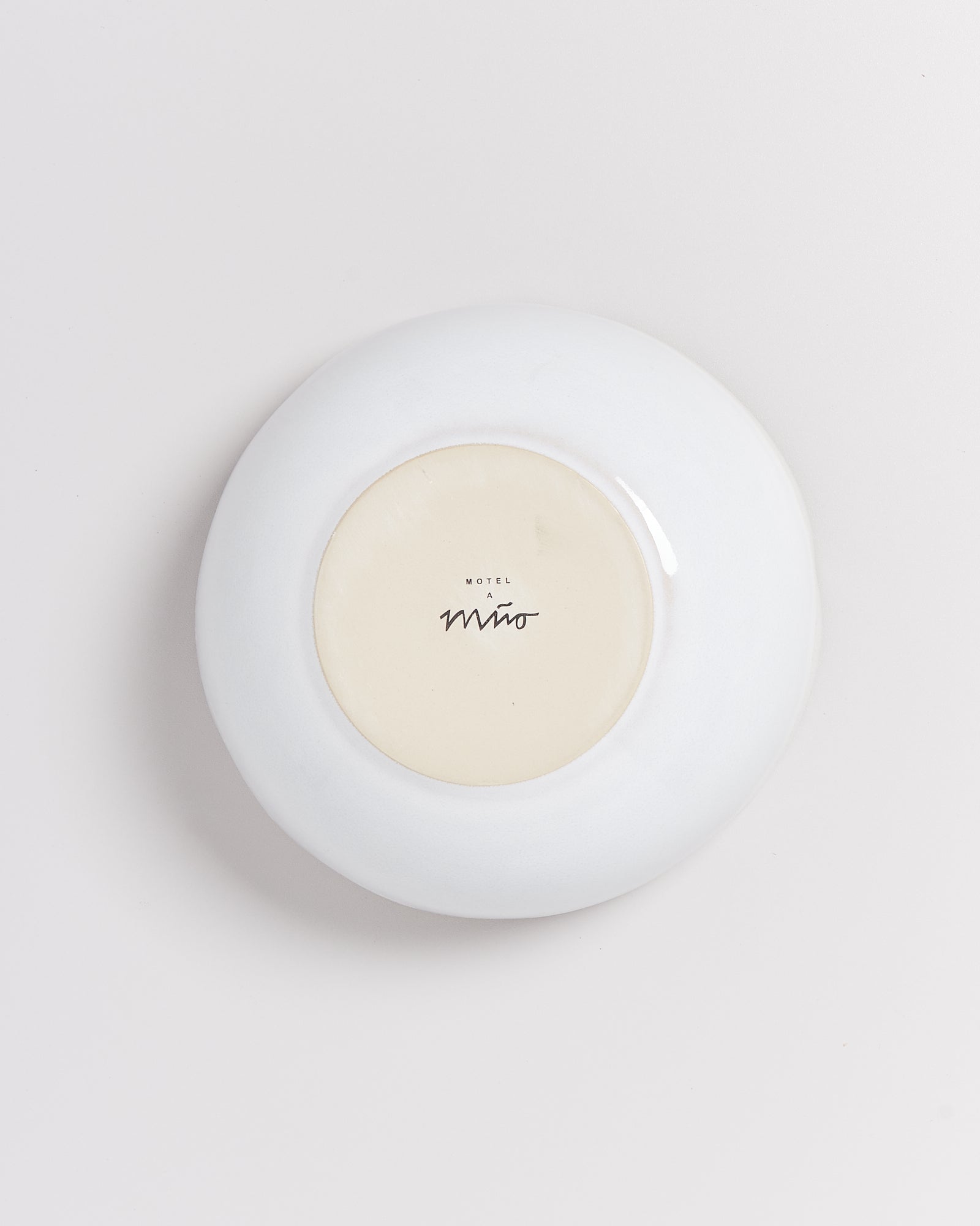 Rückseite eines weißen Tellers mit einem Logo und schwarzer Schrift auf cremefarbenem Hintergrund.