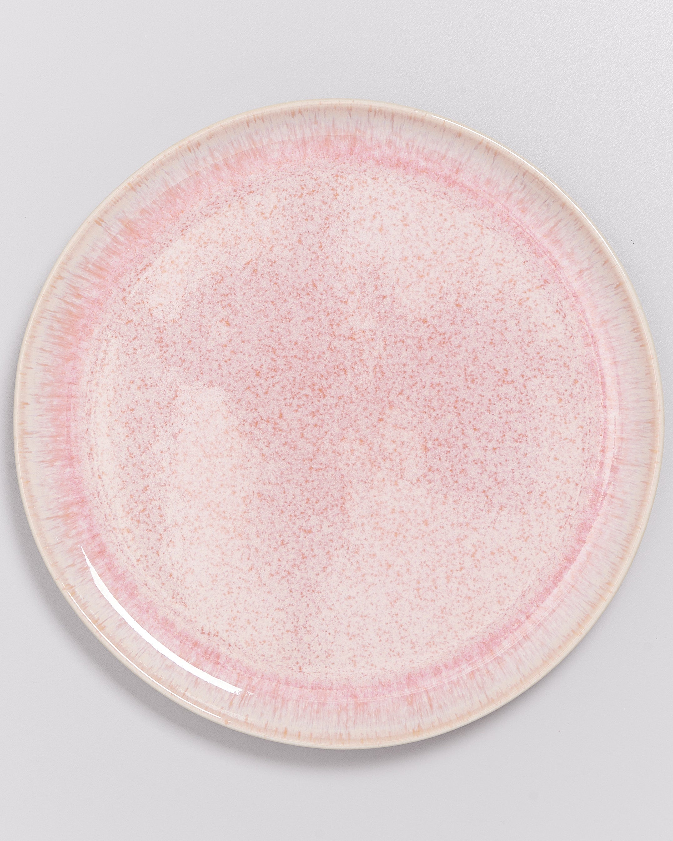 Runder Teller mit rosa Sprenkeln auf einem grauen Hintergrund.