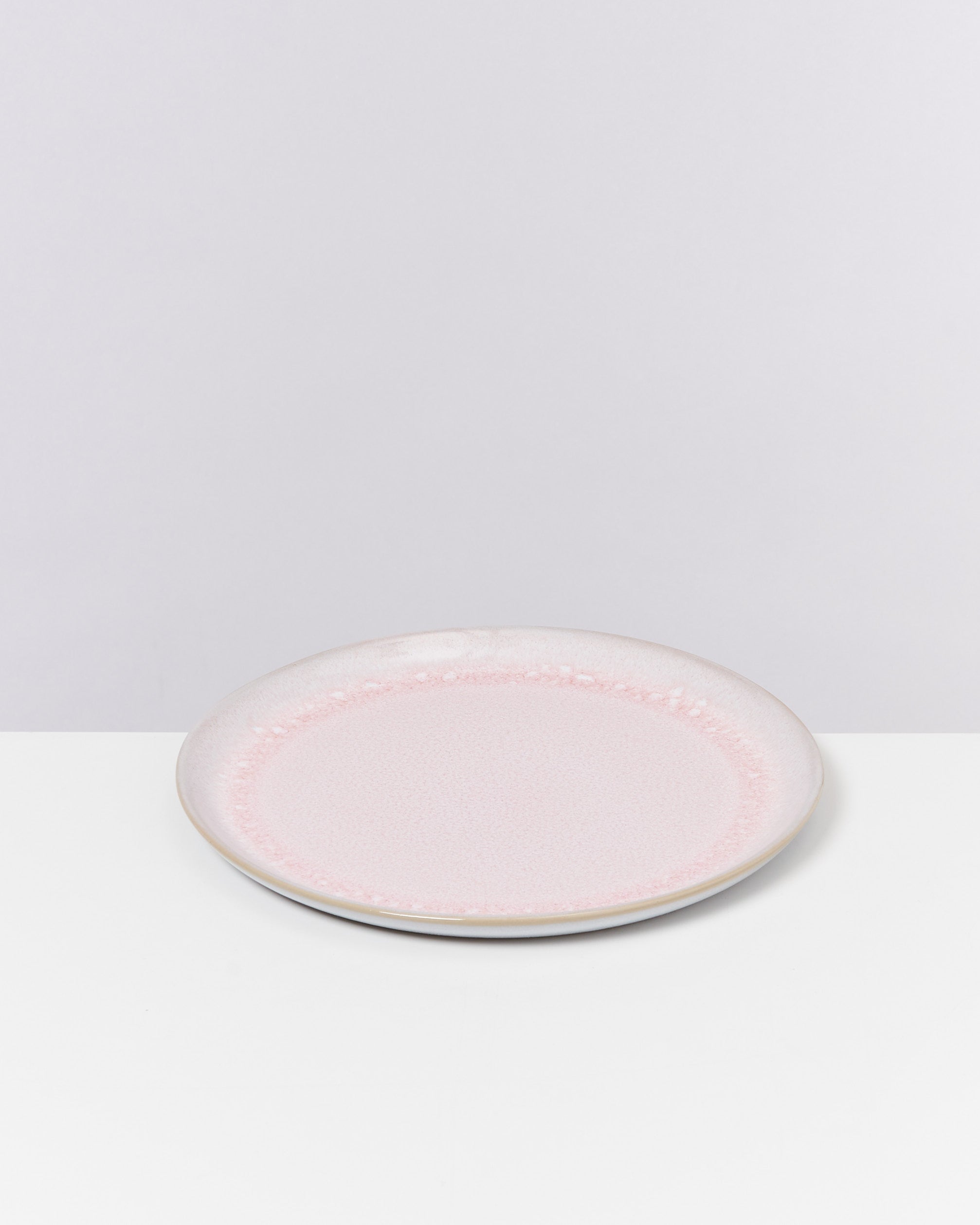 Runder, pastellrosa Teller mit feiner Struktur auf einer weißen Oberfläche vor grauem Hintergrund.