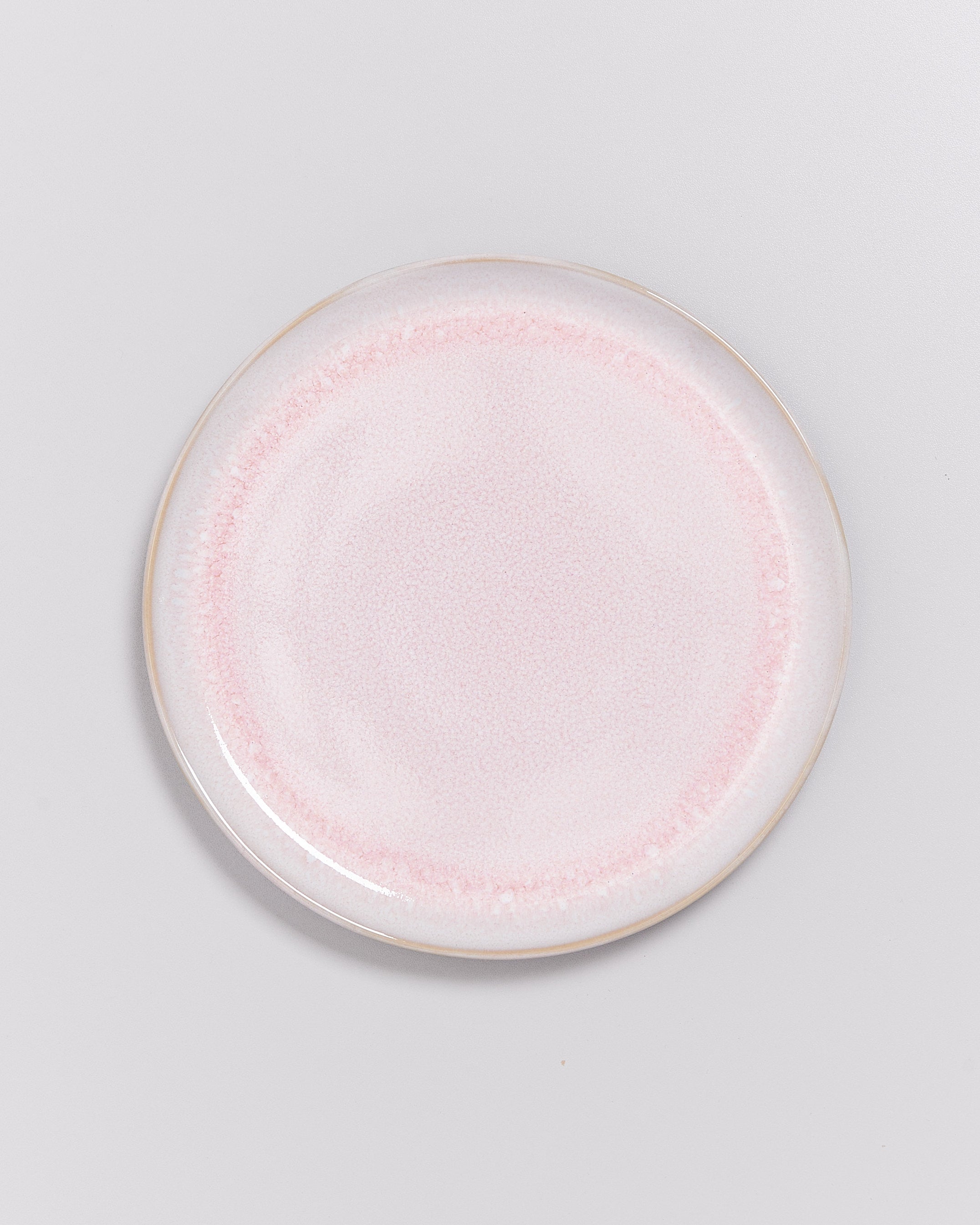 Runder, rosafarbener Keramikteller auf hellem Hintergrund.